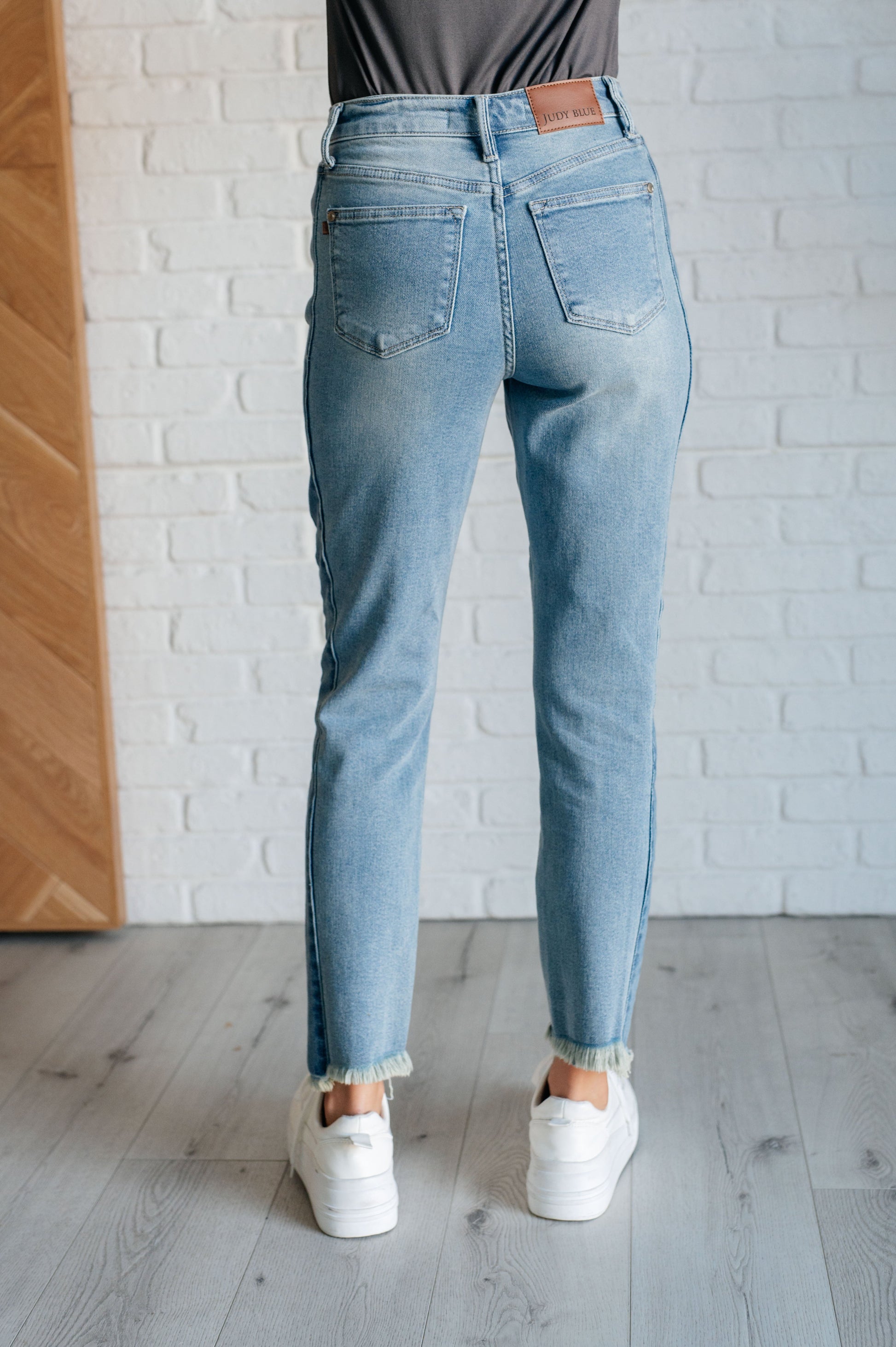 Judy Blue Susan High Rise Slim Jeans in medium wash, featuring contrast side panels, raw frayed hem, high/low stepped hem, and 4-way stretch for a sleek fit.