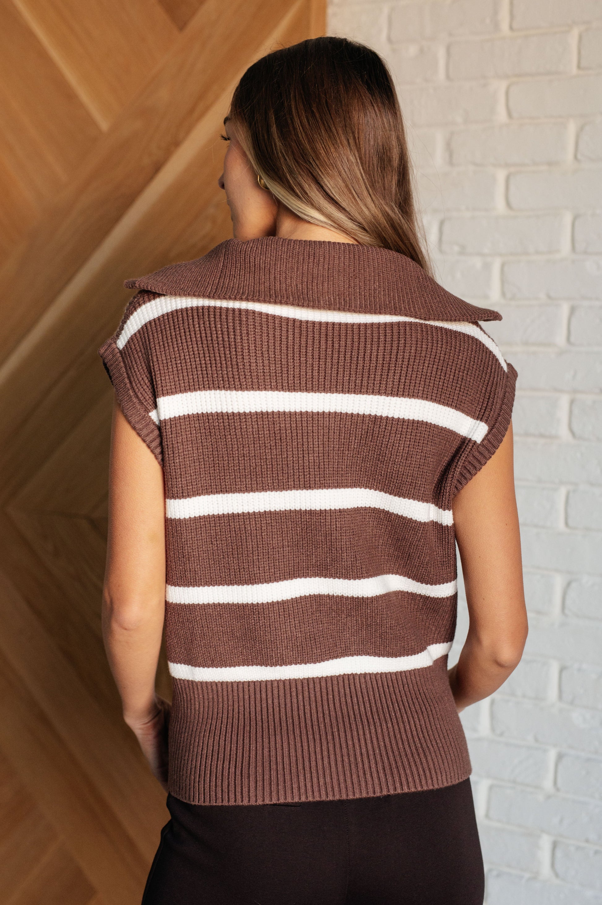 A cozy sweater vest made from mid-weight sweater knit fabric, featuring a stylish brown and off-white striped pattern. It has a high neckline with a half-zipper closure, banded ribbed sleeve cuffs, and an exaggerated banded ribbed hemline.