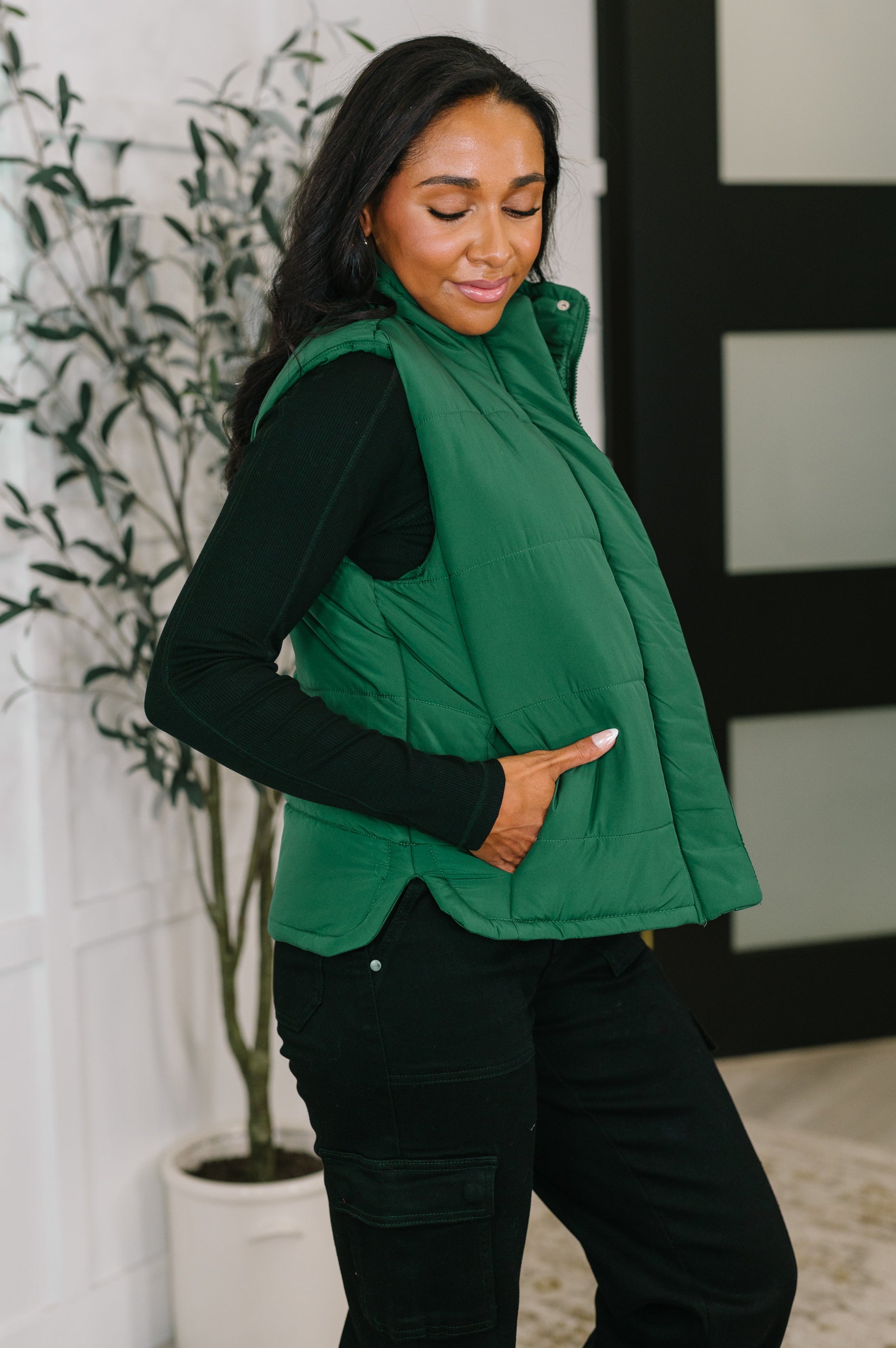Side angle of Izabella Puffer Vest in hunter green highlighting side slit and pocket.