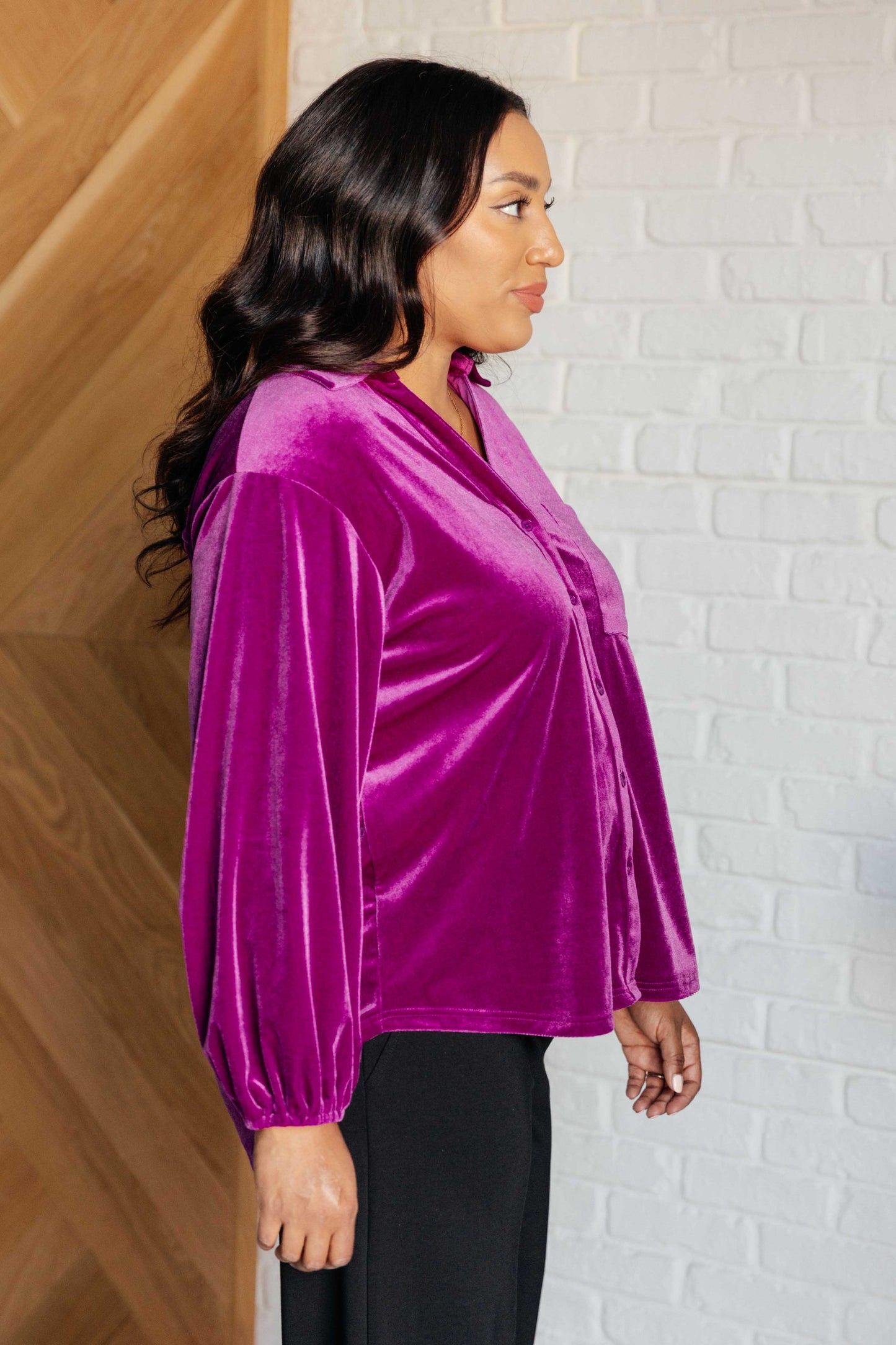 Purple velvet balloon sleeve top with a collared neckline and drop shoulder. Features long balloon sleeves with elastic cuffs, front button closures, a scooped hemline, a patch pocket, and a back gathered detail.