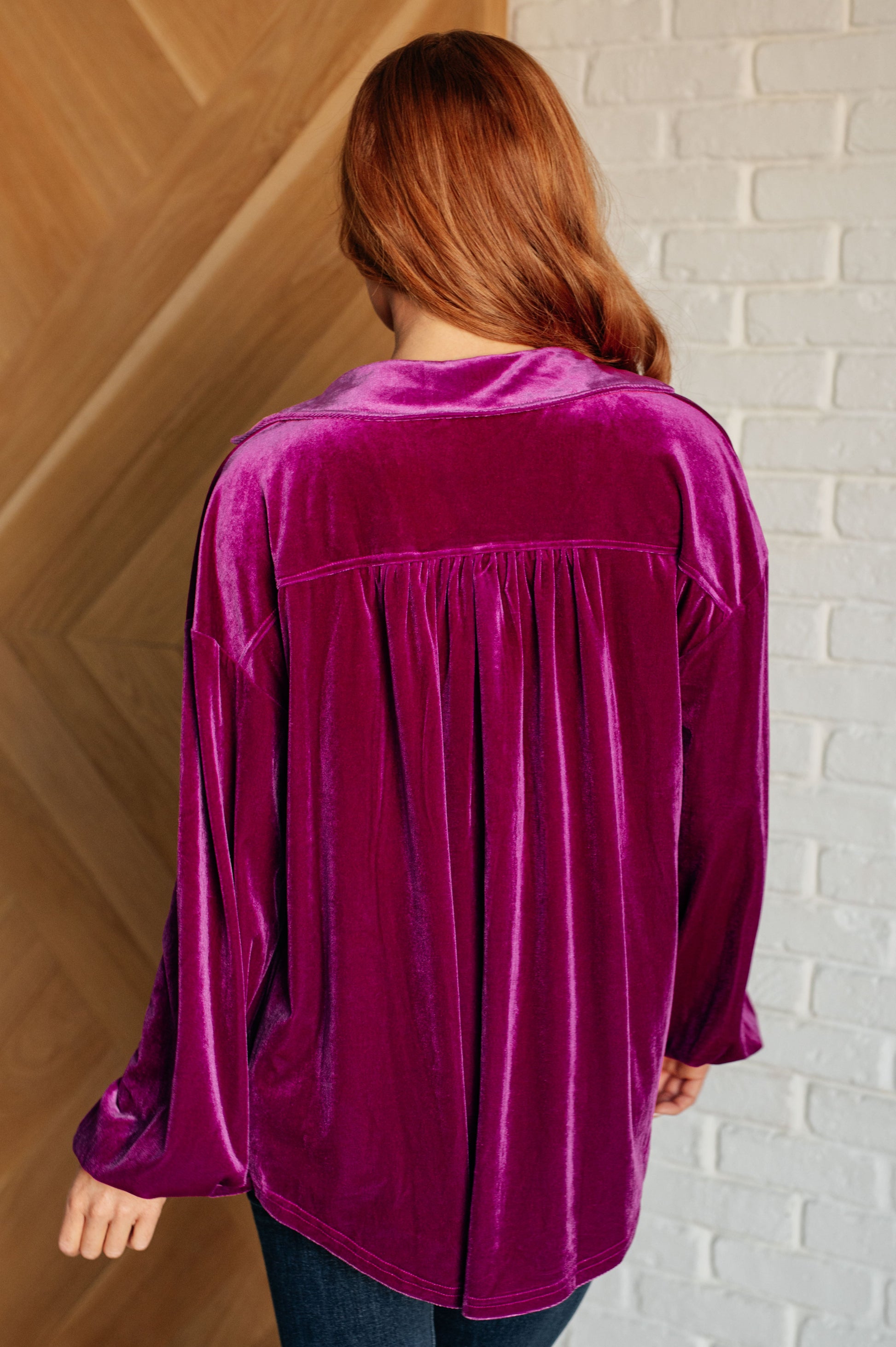 Purple velvet balloon sleeve top with a collared neckline and drop shoulder. Features long balloon sleeves with elastic cuffs, front button closures, a scooped hemline, a patch pocket, and a back gathered detail.