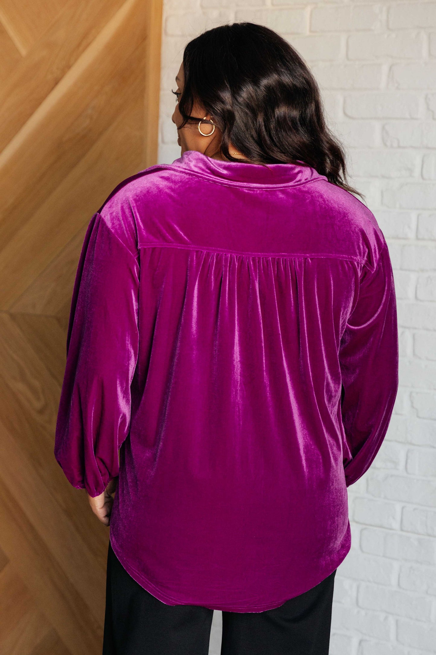 Purple velvet balloon sleeve top with a collared neckline and drop shoulder. Features long balloon sleeves with elastic cuffs, front button closures, a scooped hemline, a patch pocket, and a back gathered detail.