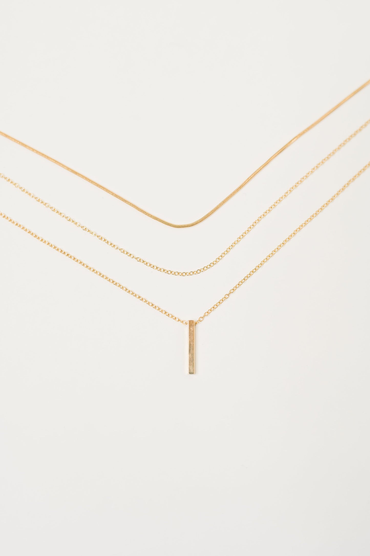 Flat lay close-up of layered gold chains with bar pendant