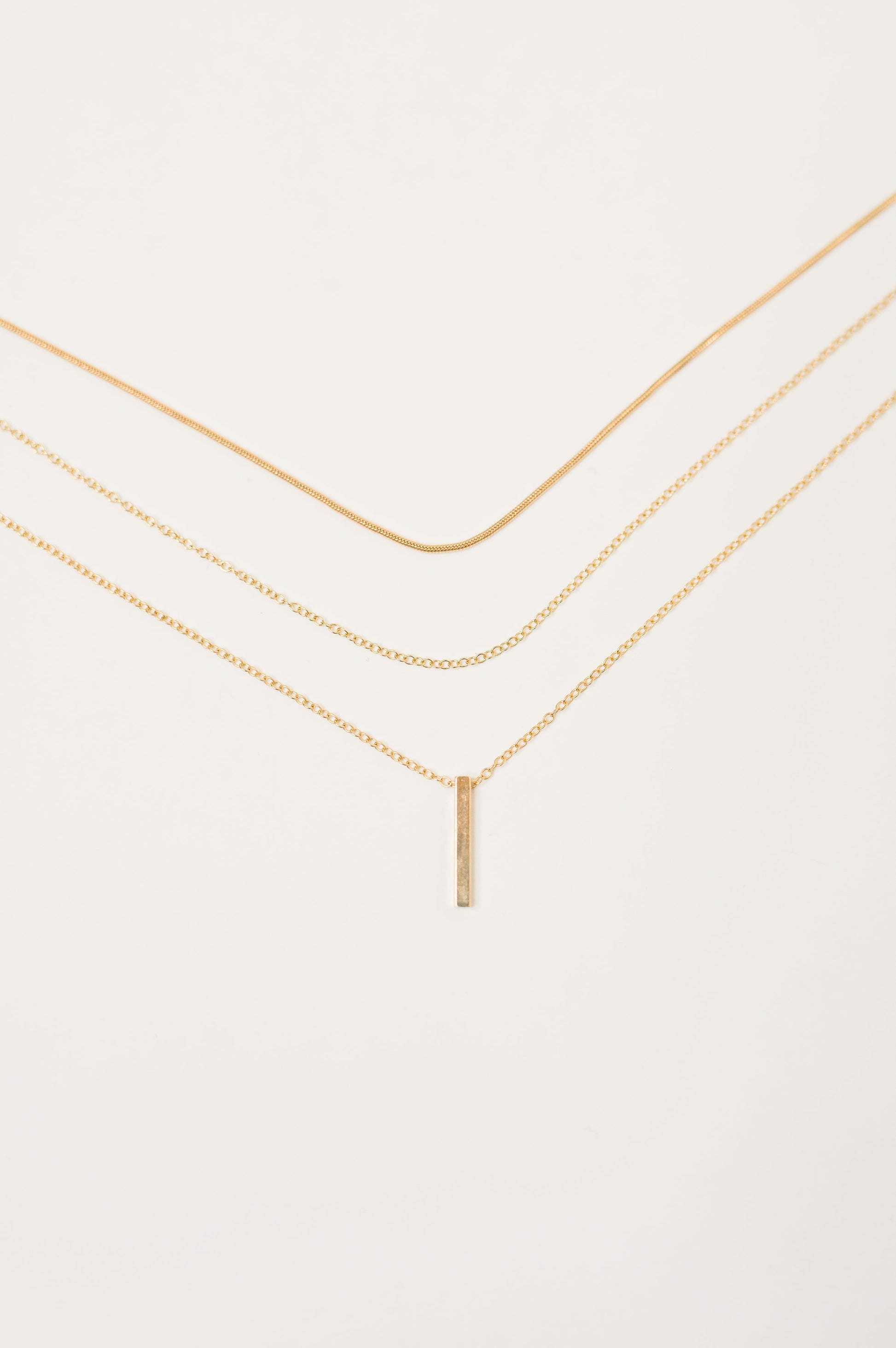 Flat lay close-up of layered gold chains with bar pendant