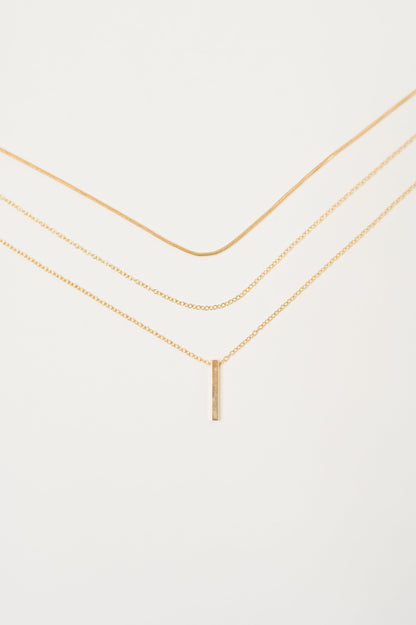 Flat lay close-up of layered gold chains with bar pendant