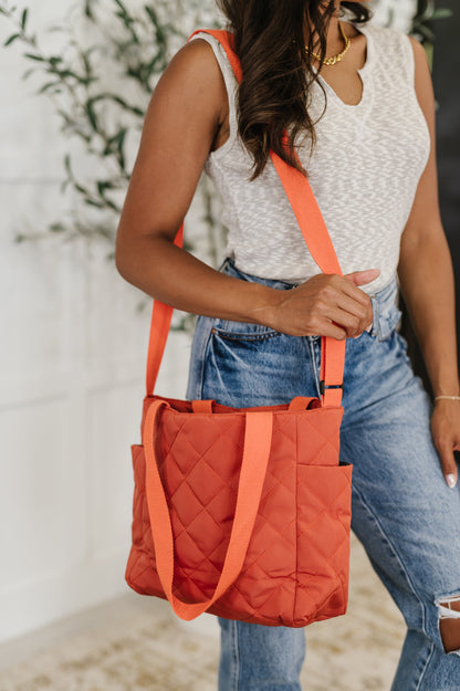 Side view of model carrying Tallulah tomato red quilted tote bag over shoulder with padded texture and roomy design