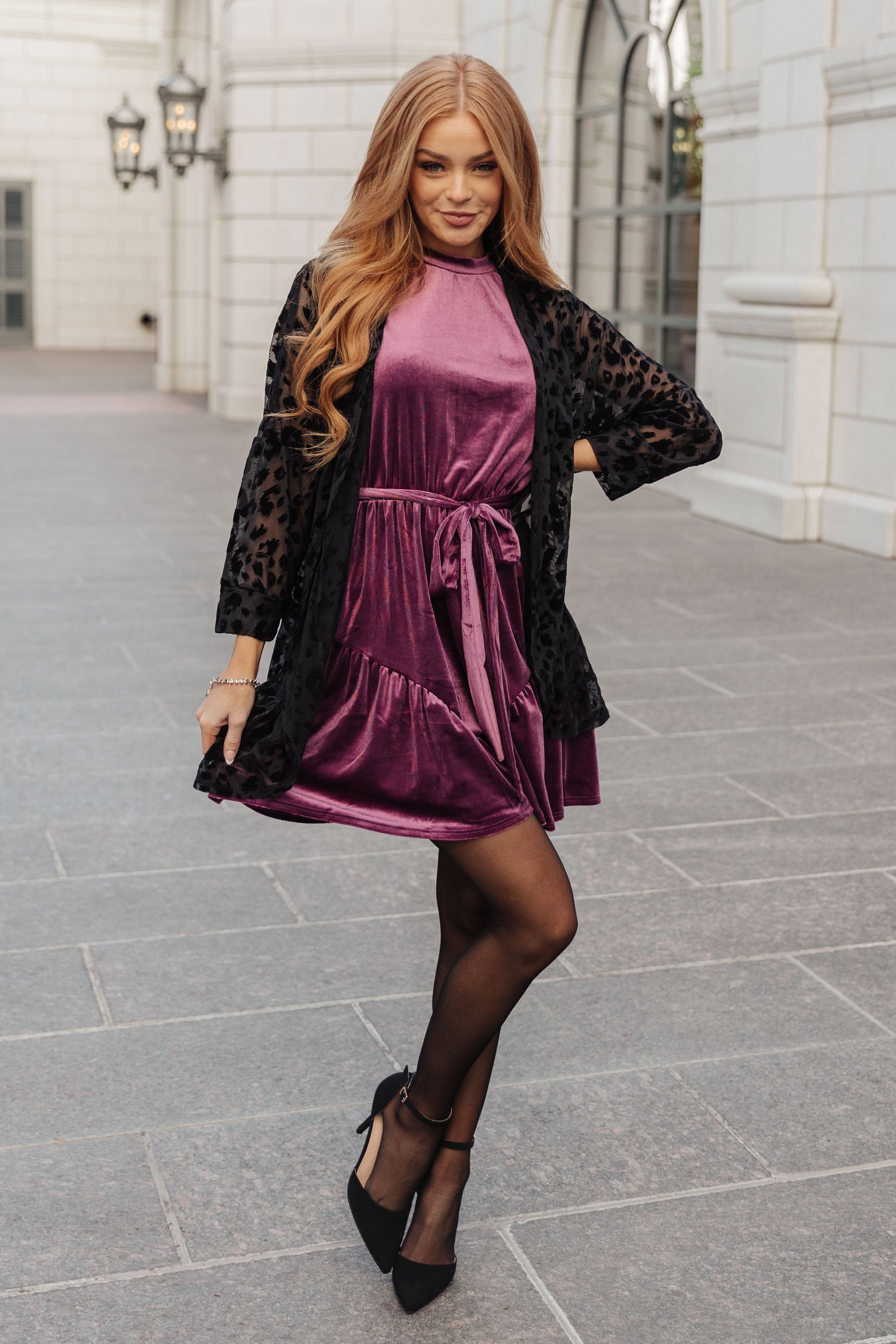 Purple velvet sleeveless dress with a mock neckline, keyhole button closure, and cased elastic waistband. Features a removable self-tie belt, ruffled hem, and is fully lined.