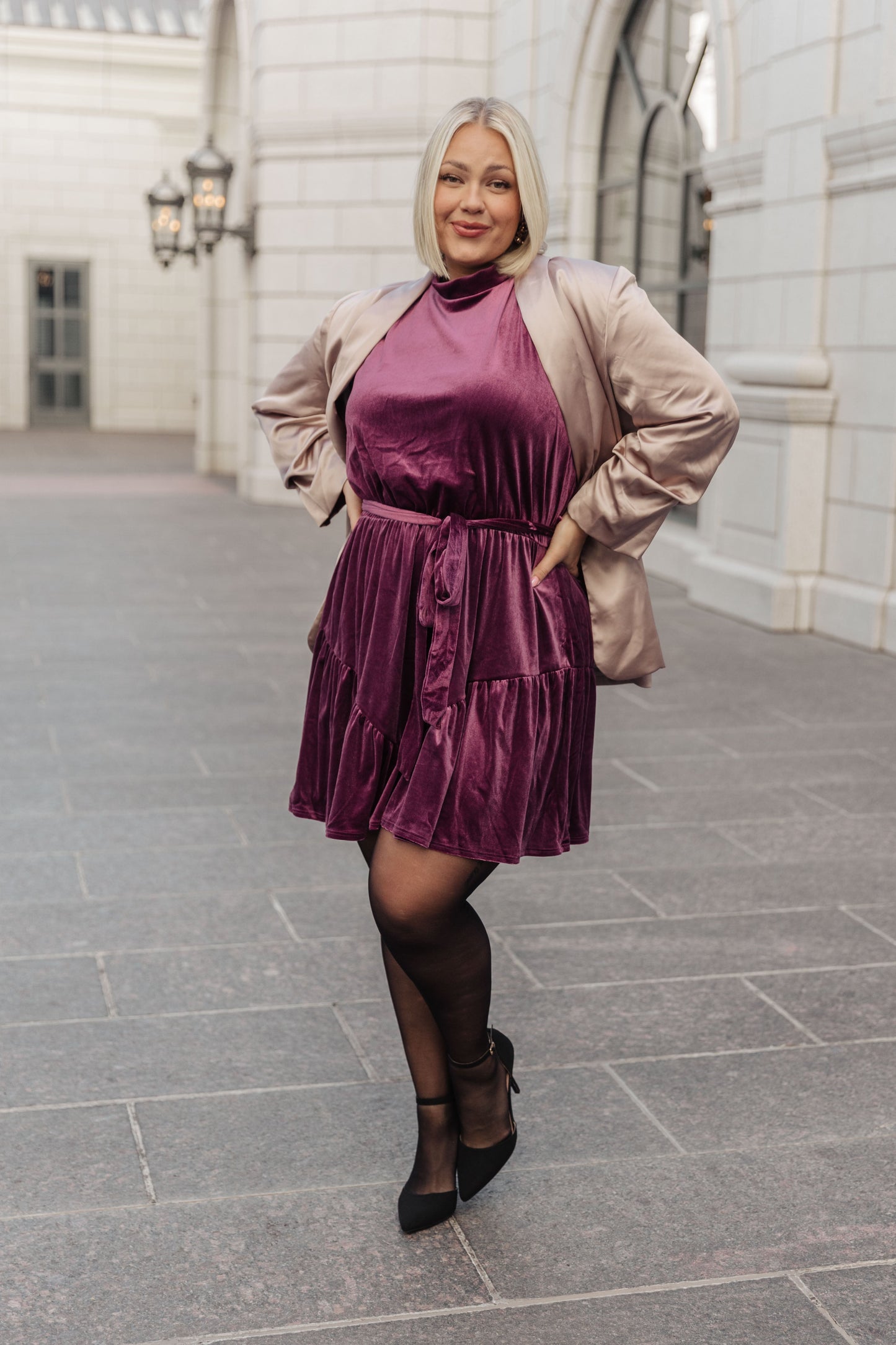 Purple velvet sleeveless dress with a mock neckline, keyhole button closure, and cased elastic waistband. Features a removable self-tie belt, ruffled hem, and is fully lined.