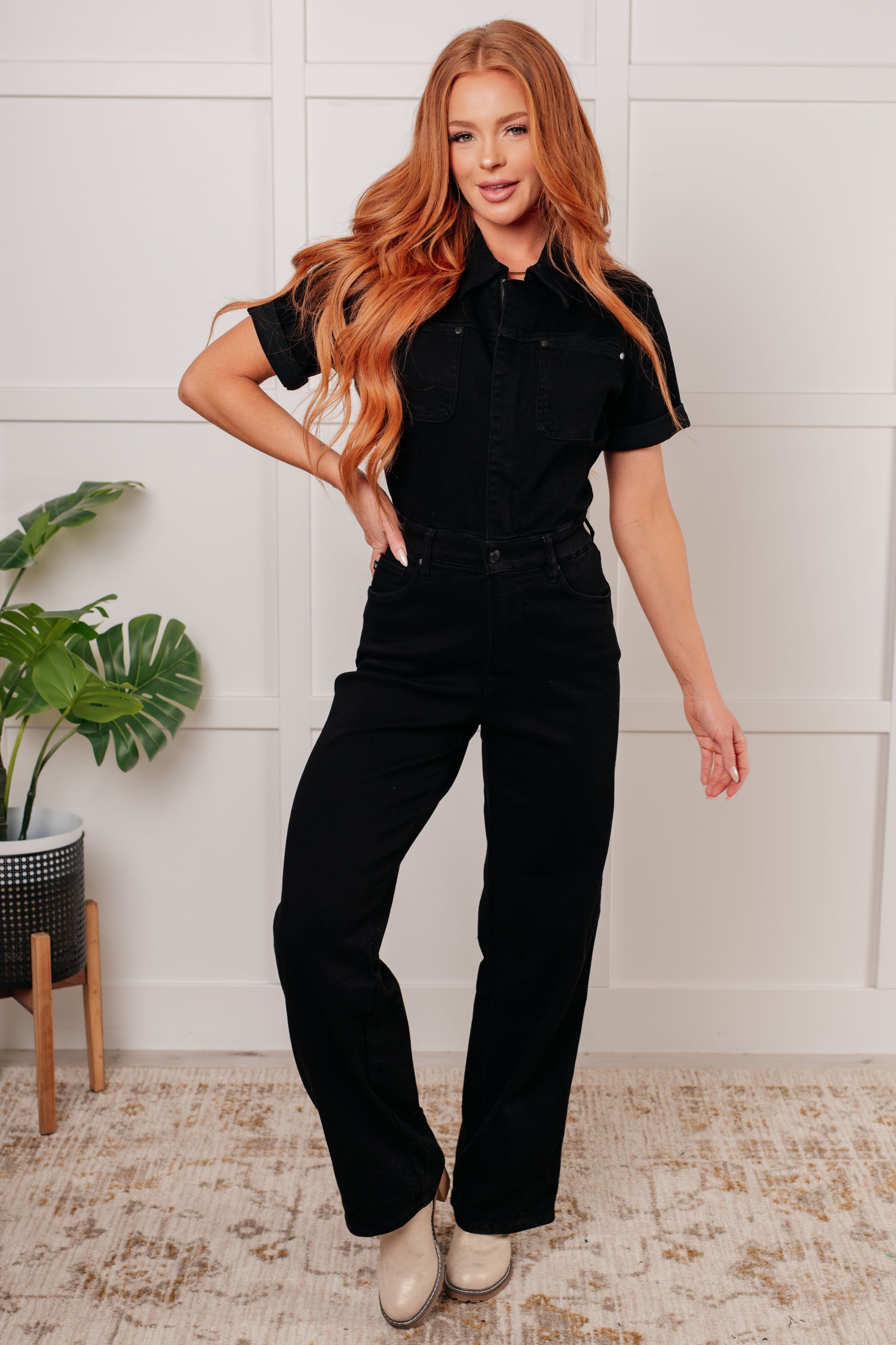 Judy Blue black garment-dyed denim jumpsuit with a collared neckline, short sleeves, and high-rise waist. Features a tummy control panel, 4-way stretch, and front and back pockets. Zipper front with snap waistband and straight-leg silhouette.