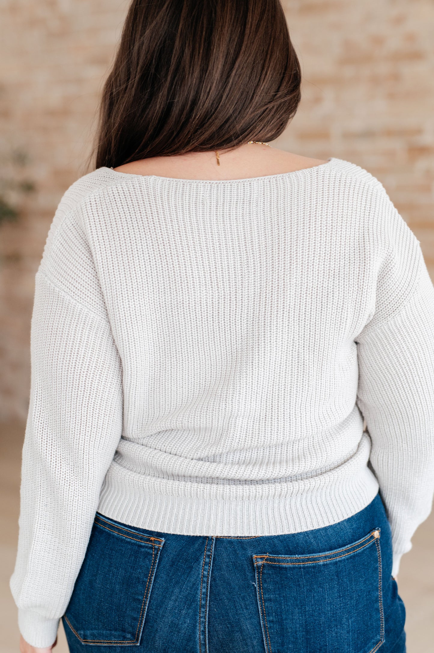 Women's light gray slim fit sweater with a V-neckline and long sleeves, made from lightweight sweater knit fabric.