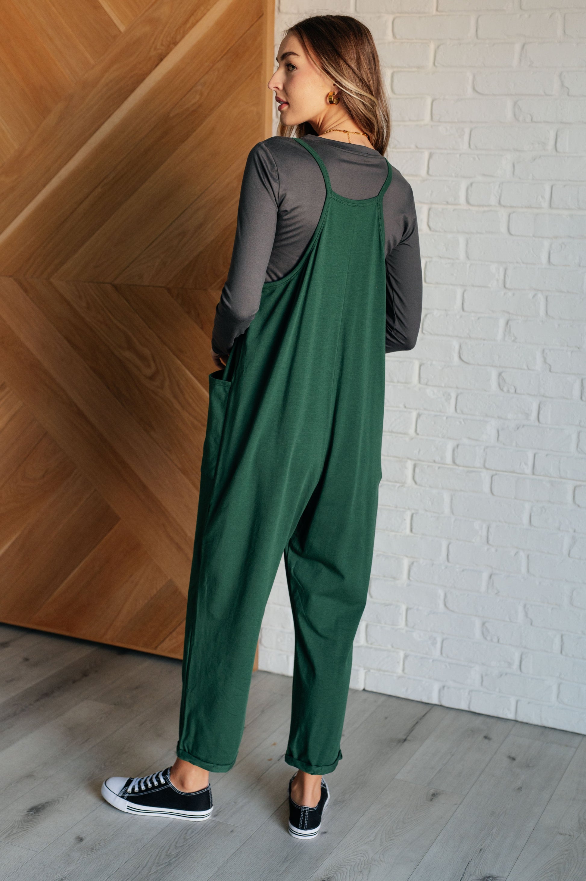 Dark green spaghetti strap jumpsuit with a scooped neckline, patch pockets, and tacked cuffs at the hem.