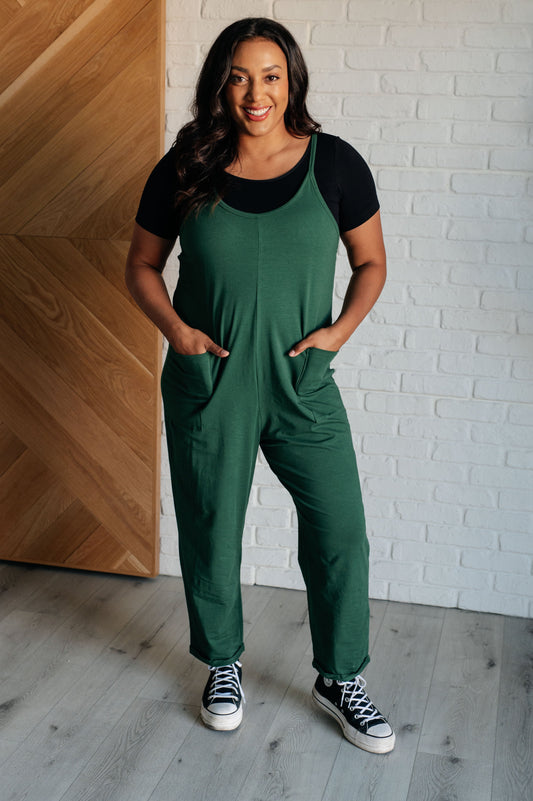 Dark green spaghetti strap jumpsuit with a scooped neckline, patch pockets, and tacked cuffs at the hem.