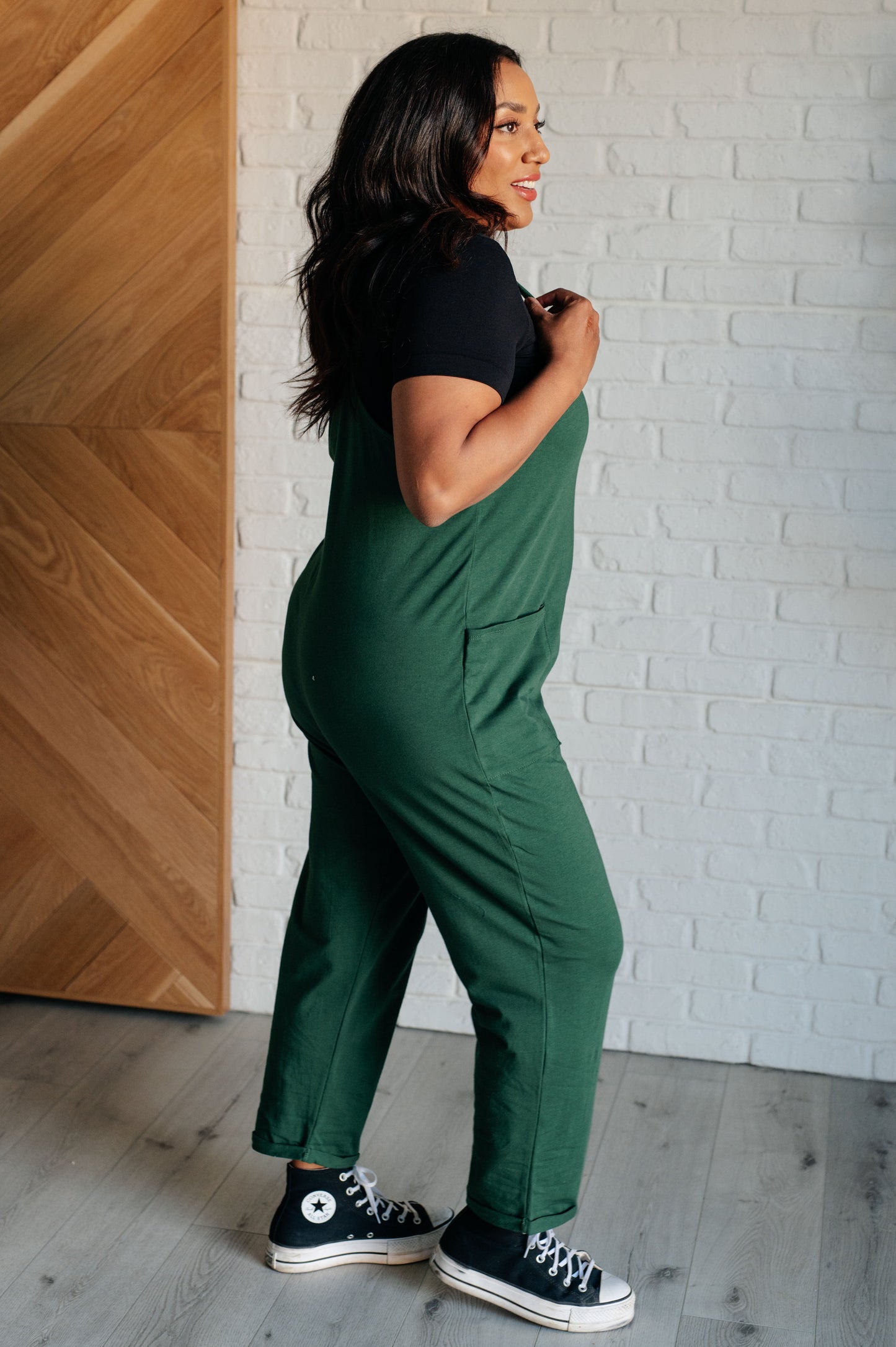 Dark green spaghetti strap jumpsuit with a scooped neckline, patch pockets, and tacked cuffs at the hem.