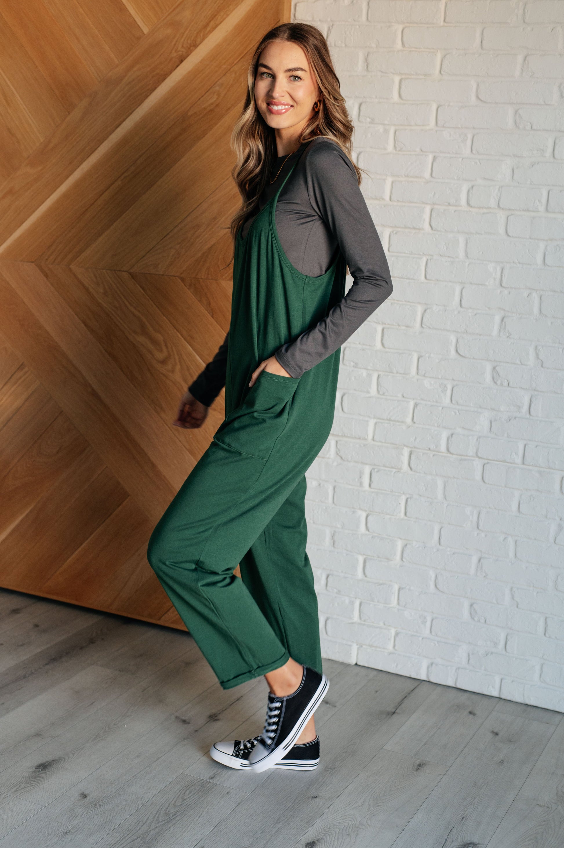 Dark green spaghetti strap jumpsuit with a scooped neckline, patch pockets, and tacked cuffs at the hem.