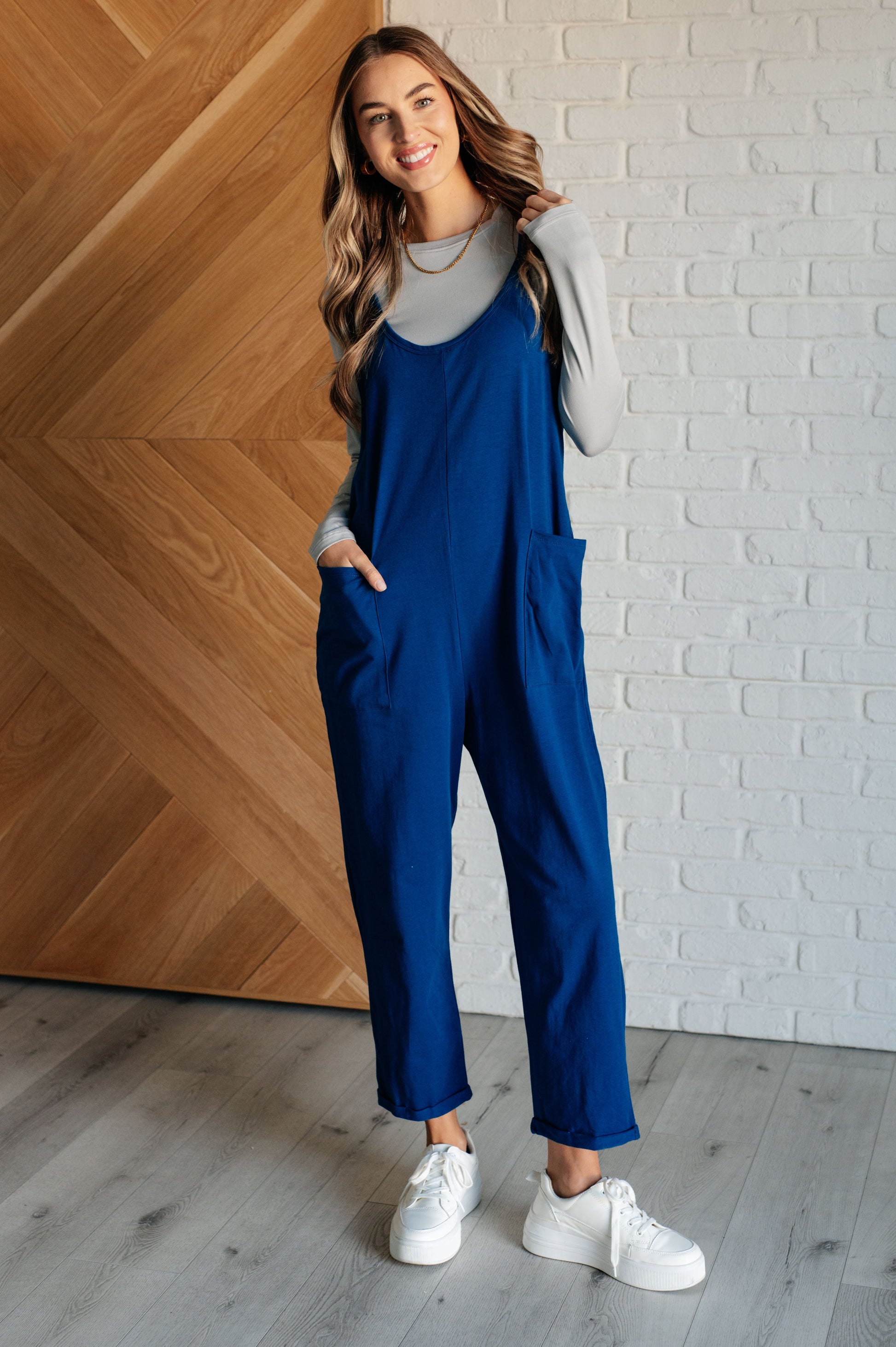 Light Navy spaghetti strap jumpsuit with a scooped neckline, patch pockets, and tacked cuffs at the hem.