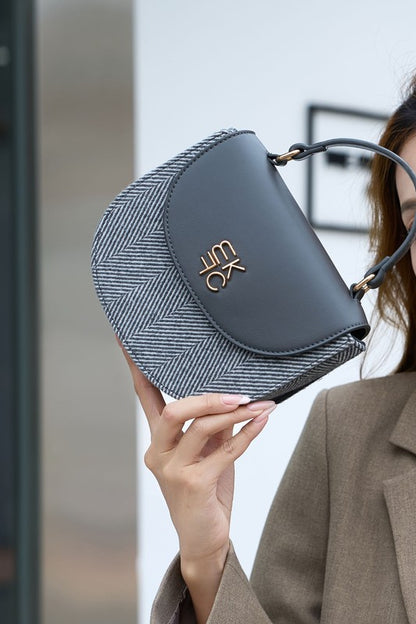 Woman holding gray Heloise herringbone crossbody bag showing size and handle.