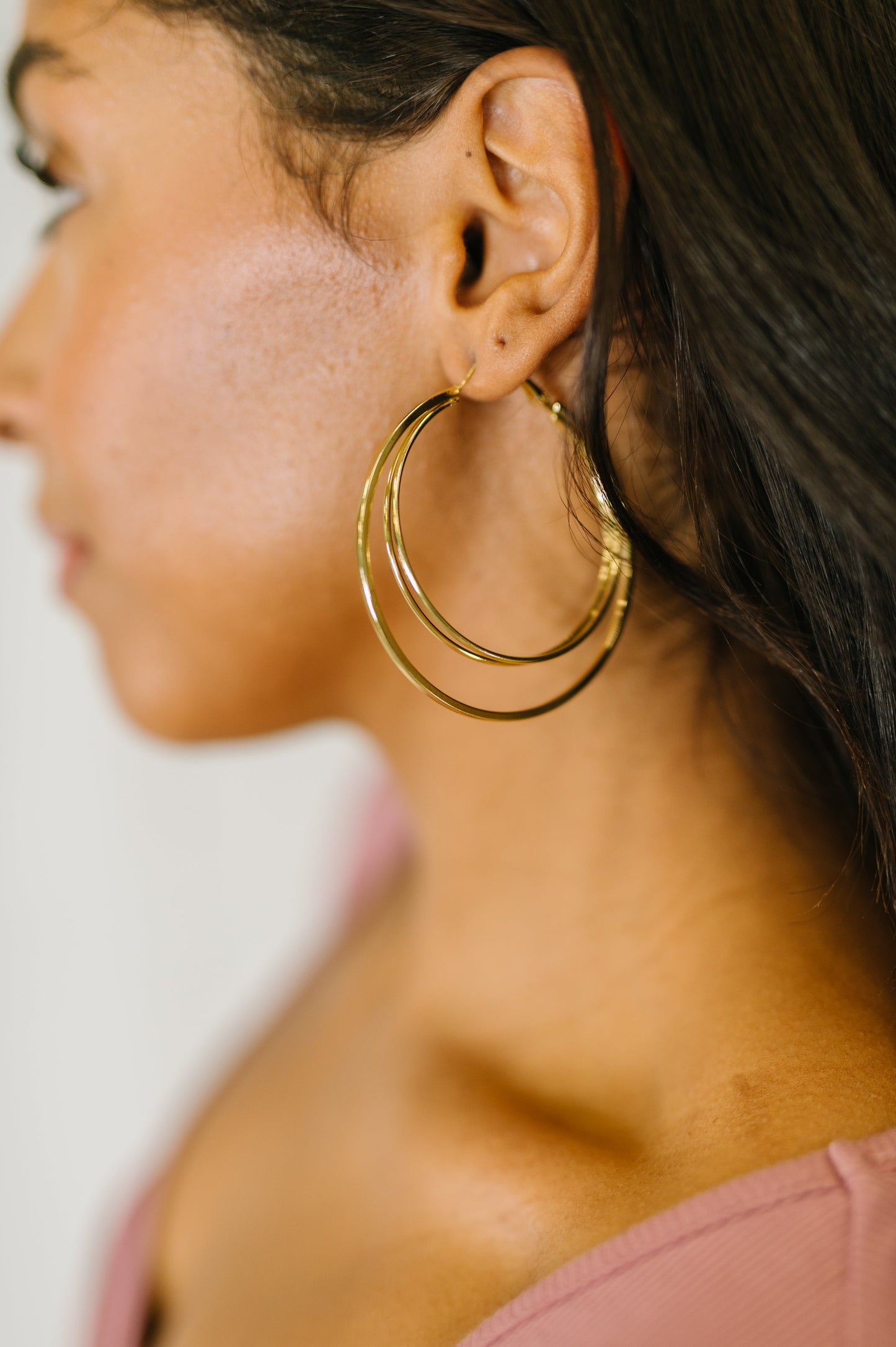 Close-up of a person wearing the Two's a Party - gold double hoop earrings with hinge closure.