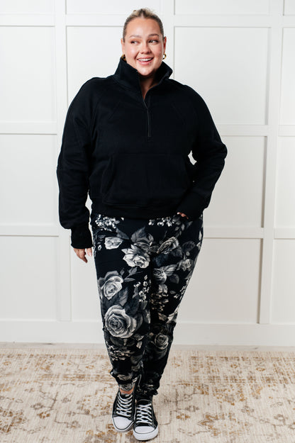 Plus size model full body view of Sara Half Zip Pullover in black paired with floral joggers.