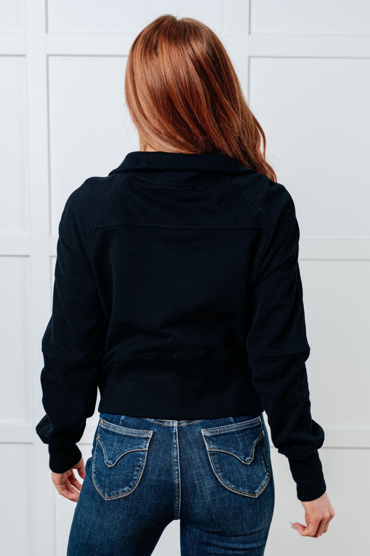 A women's pullover made from soft black terry cloth, featuring a high neckline with a half-zip closure, raglan long sleeves with thumbholes, banded ribbed cuffs and hem, and a kangaroo pocket.