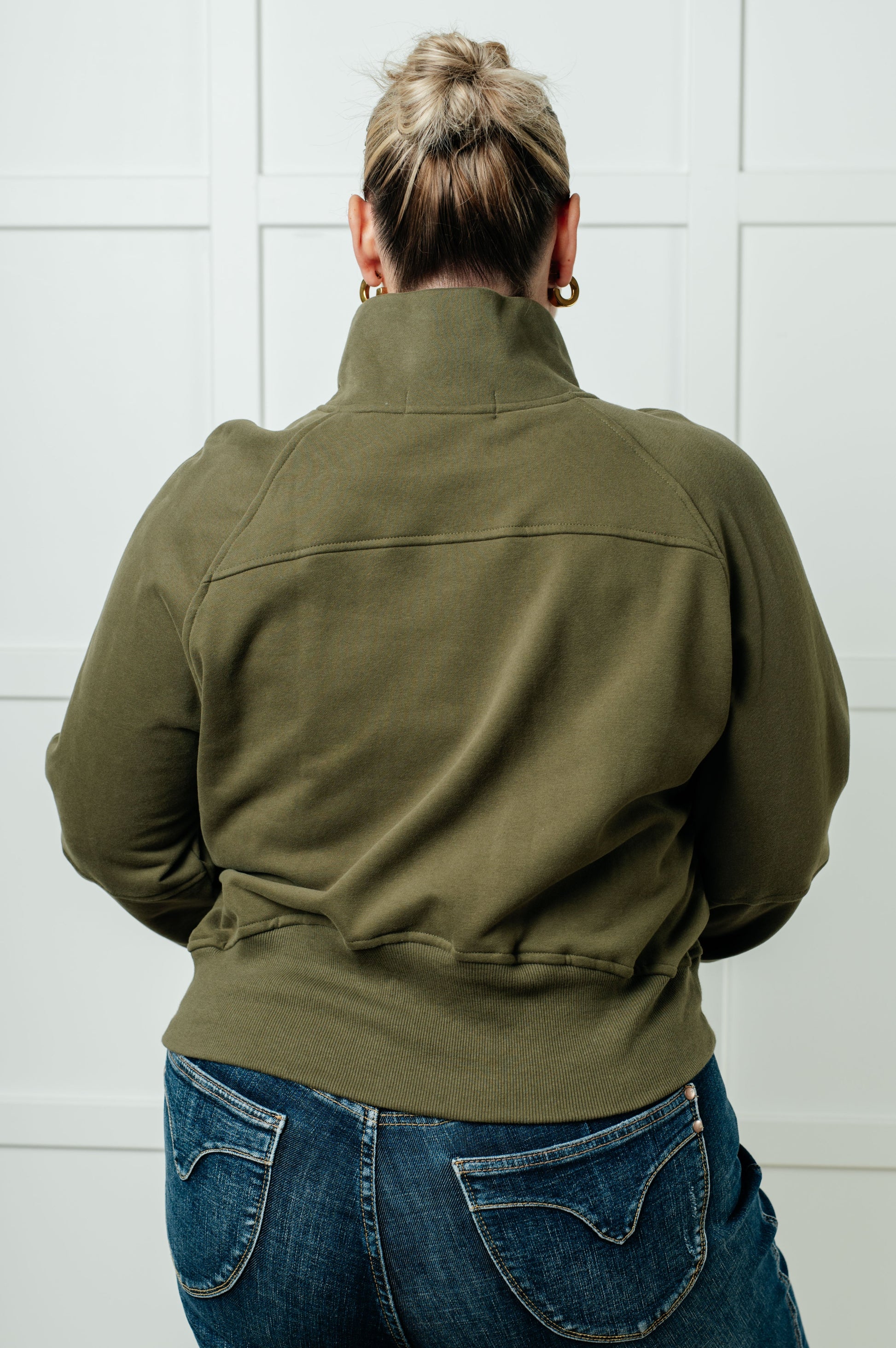 A women's pullover made from soft green terry cloth, featuring a high neckline with a half-zip closure, raglan long sleeves with thumbholes, banded ribbed cuffs and hem, and a kangaroo pocket.