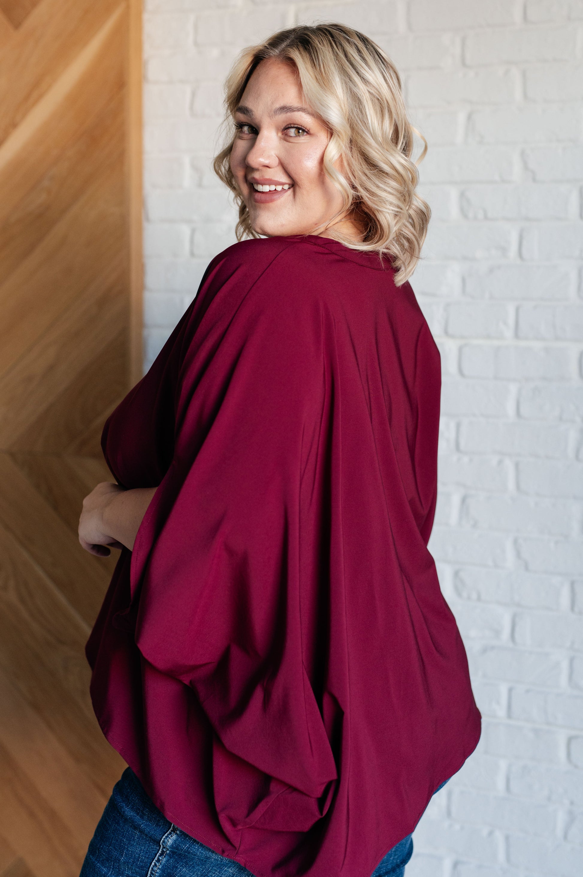 Women's wine-colored poncho-style blouse with a Gabby V-neckline, batwing sleeves, and an oversized fit, made from lightweight woven fabric.