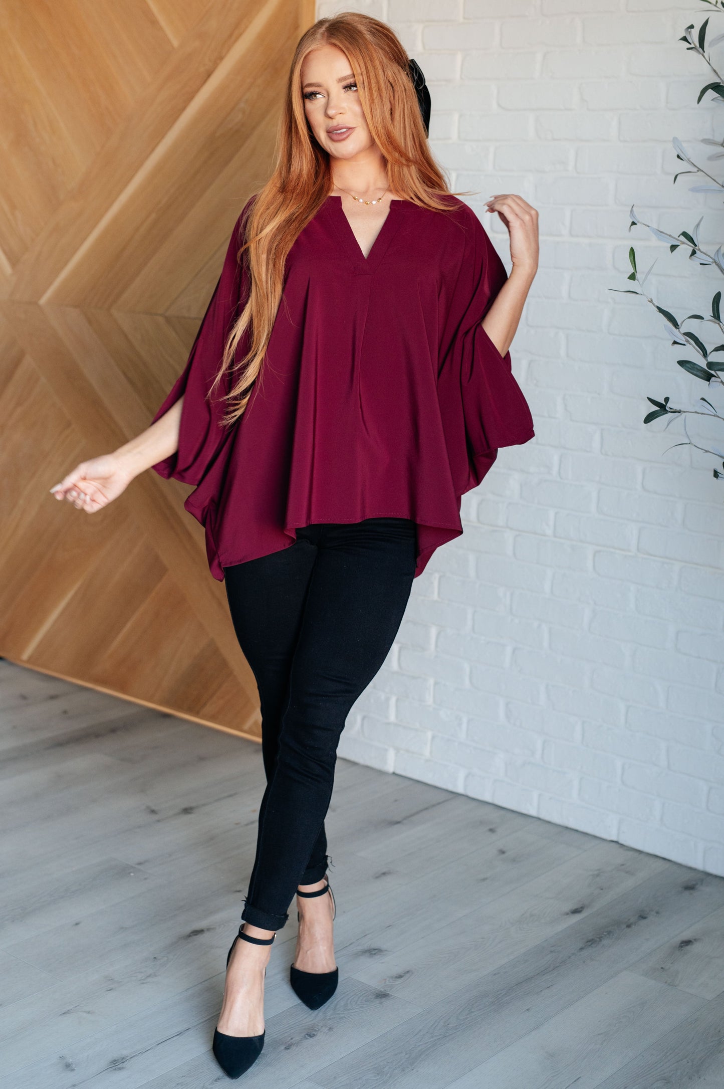 Women's wine-colored poncho-style blouse with a Gabby V-neckline, batwing sleeves, and an oversized fit, made from lightweight woven fabric.