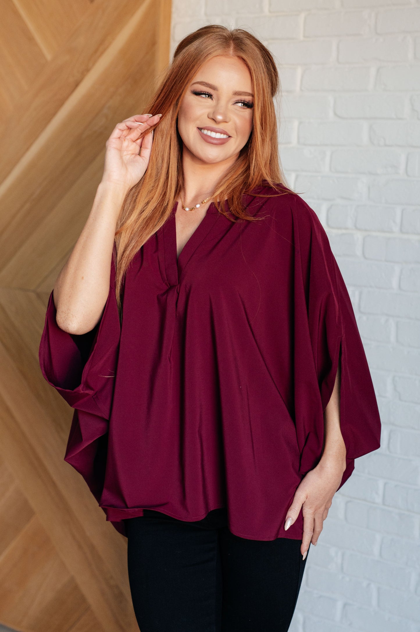 Women's wine-colored poncho-style blouse with a Gabby V-neckline, batwing sleeves, and an oversized fit, made from lightweight woven fabric.