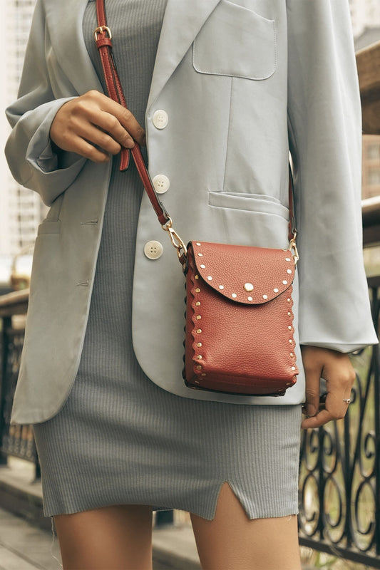 Woman holding brown Filomena crossbody bag with gold hardware and adjustable strap.