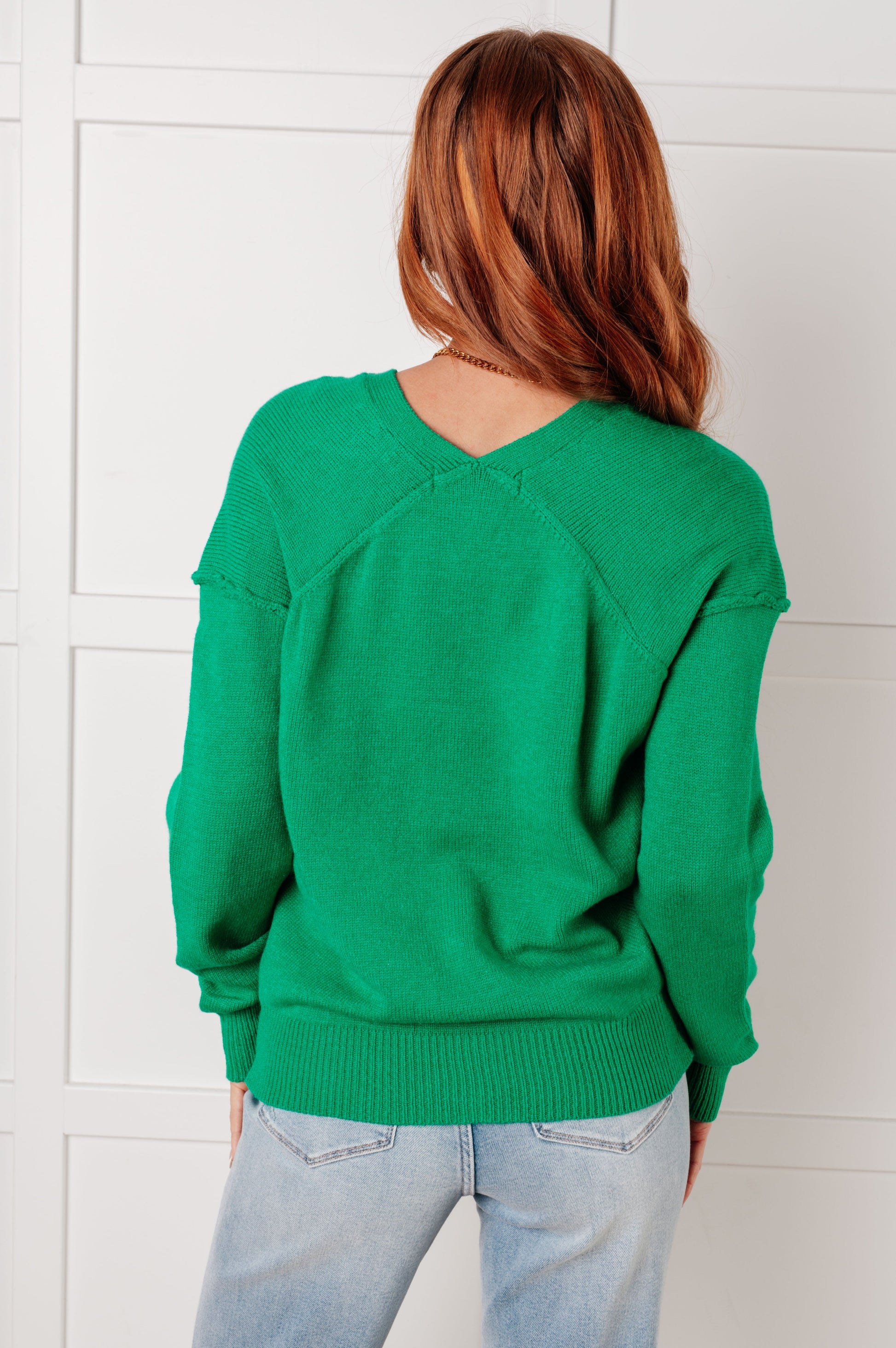 Back view of a model wearing the Veru V-Neck Sweater in Green with ribbed cuffs and hem, drop shoulder design, exposed seams, and lightweight knit fabric, perfect for layering or standalone wear.