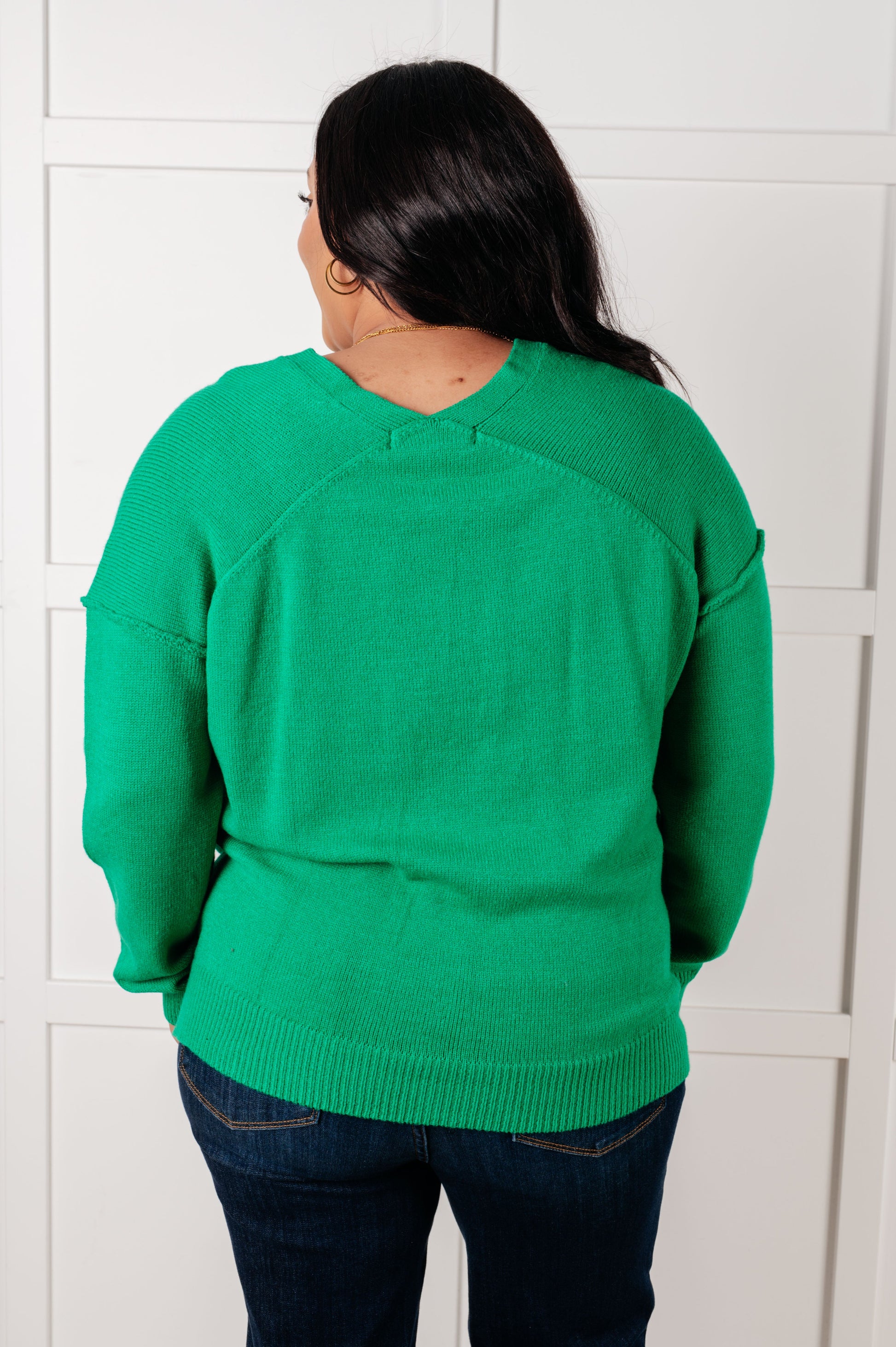 Back view of a plus size model wearing the Veru V-Neck Sweater in Green with ribbed cuffs and hem, drop shoulder design, exposed seams, and lightweight knit fabric, perfect for layering or standalone wear.