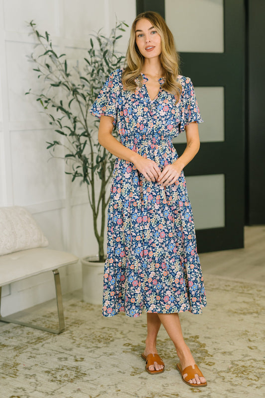 Model wearing Wania Notch Neck Midi Dress navy floral with flutter sleeves and tiered skirt.
