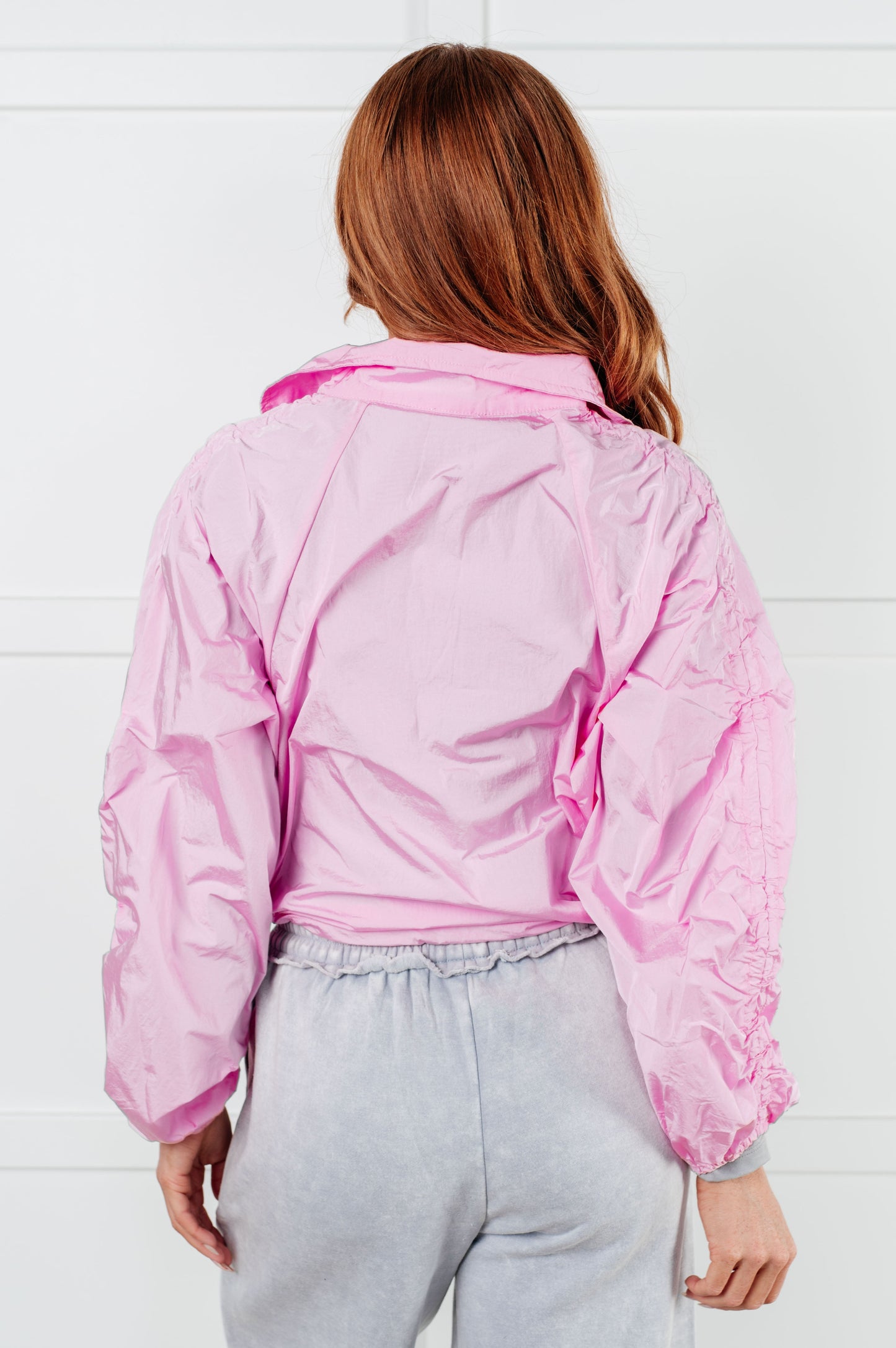 Women's pink windbreaker featuring ruched sleeves, chic collar, front zipper, adjustable hemline, and front pockets, designed for style and practicality.