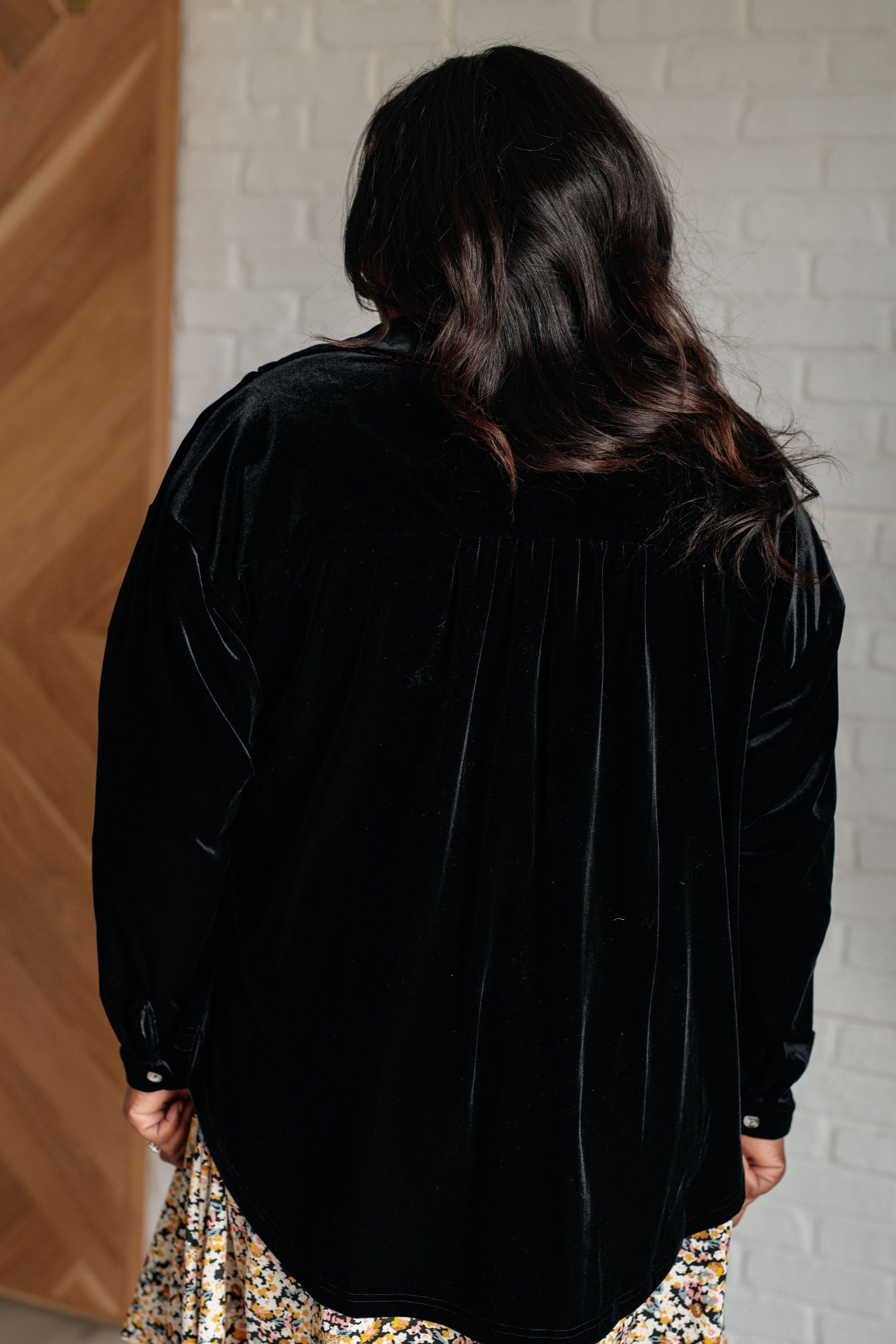 Black velvet knit button-down top with a collared neckline, long sleeves, and breast flap pockets. Features front button closure, buttoned sleeve cuffs, and a scooped hemline.