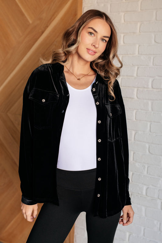 Black velvet knit button-down top with a collared neckline, long sleeves, and breast flap pockets. Features front button closure, buttoned sleeve cuffs, and a scooped hemline.