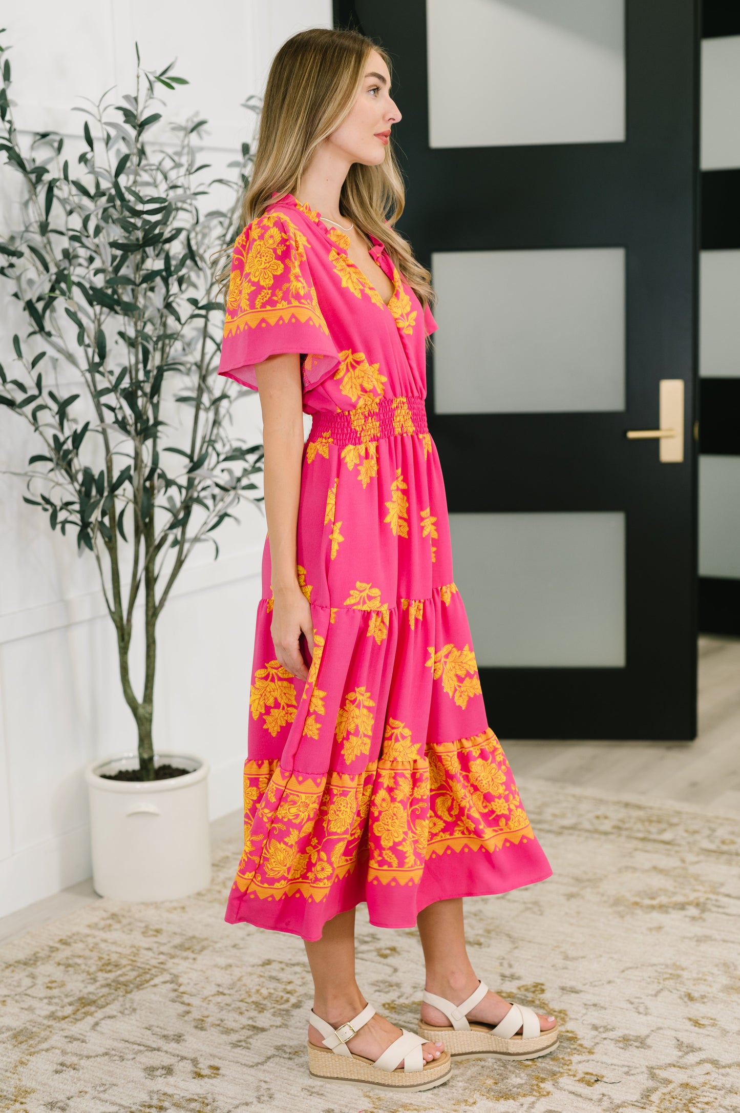 Side view of model wearing the Lainey V-Neck Dress in fuchsia, highlighting the flutter sleeve, smocked waist, and flowing tiered skirt.