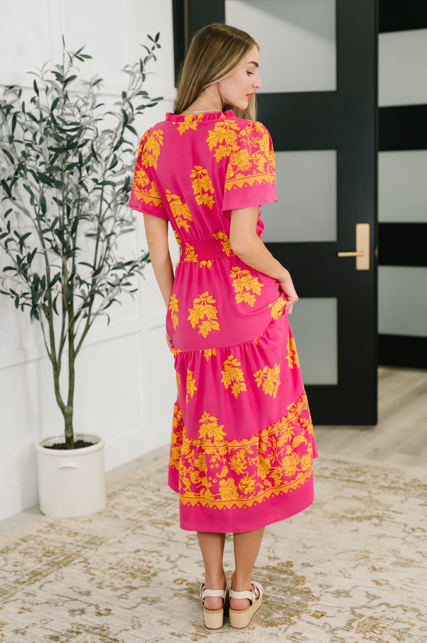 Back view of model wearing the Lainey V-Neck Dress in fuchsia, showcasing the gathered tiered skirt and flutter sleeve detail.
