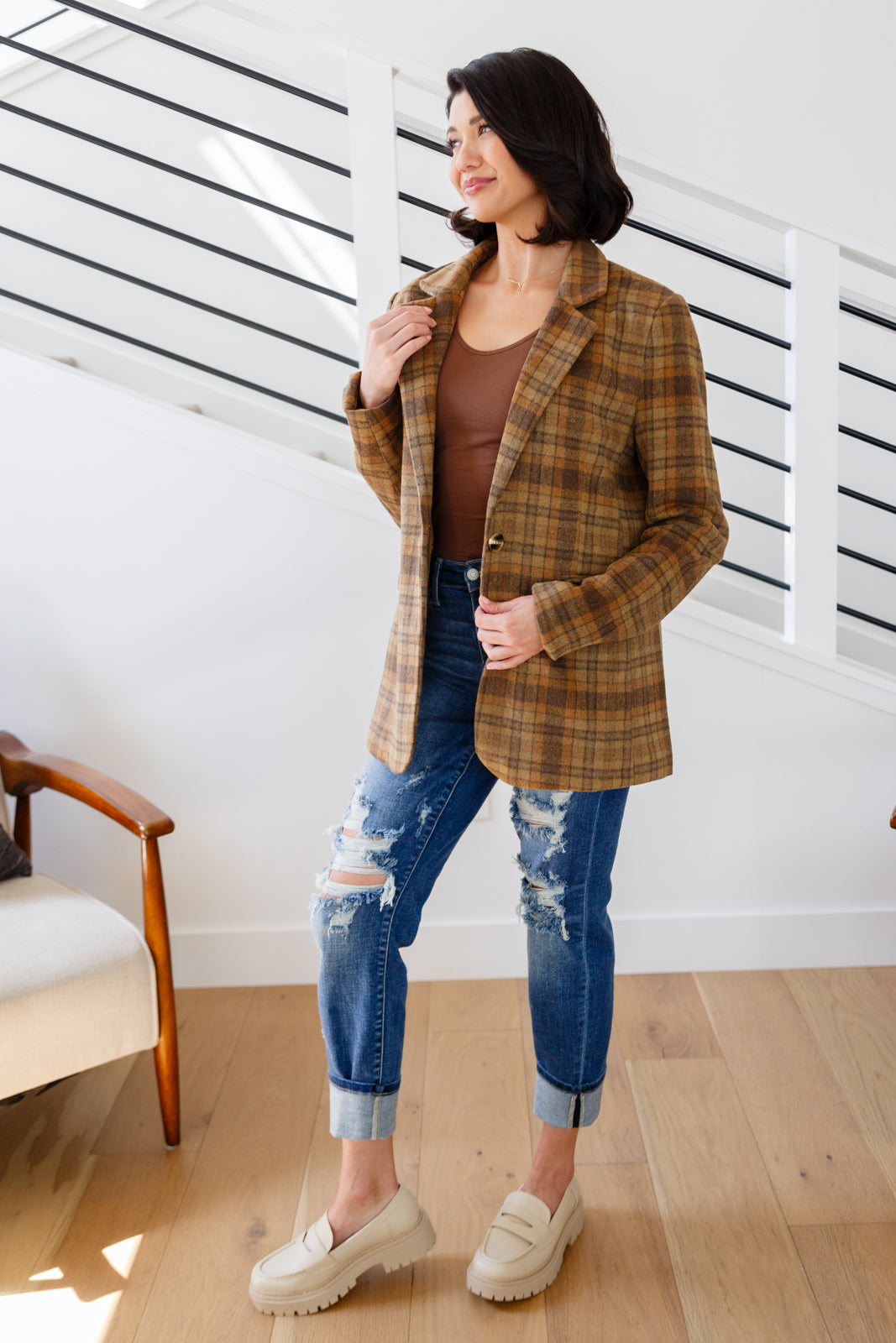 Brown plaid blazer with notched lapels, single button closure, and flap pockets. Features shoulder pads, a fully lined interior, and a tailored, relaxed fit.