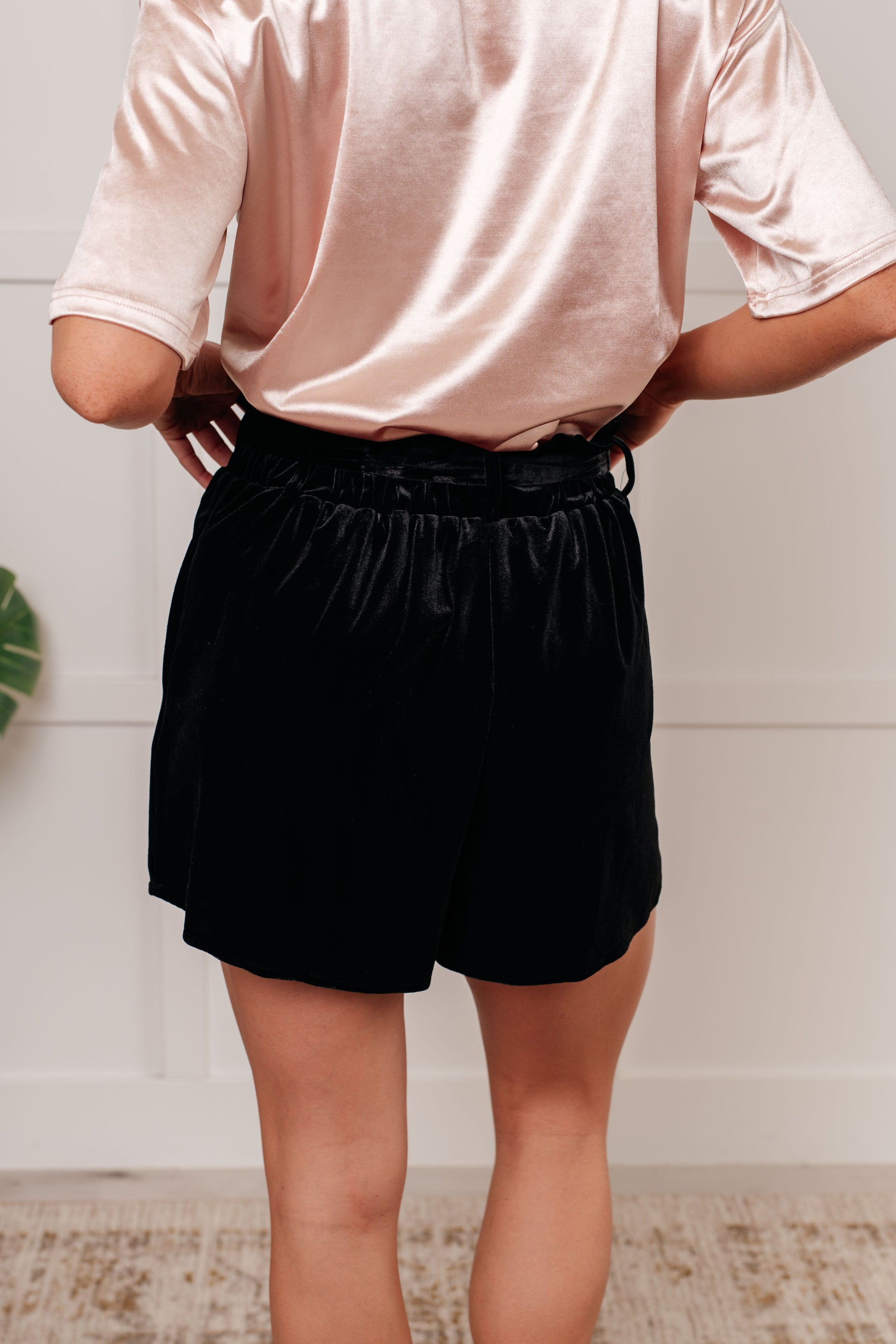 Wrapped in Velvet Shorts in black, featuring a high-rise elastic paper bag waistband, self-tie belt, and pockets for a stylish and adjustable fit.