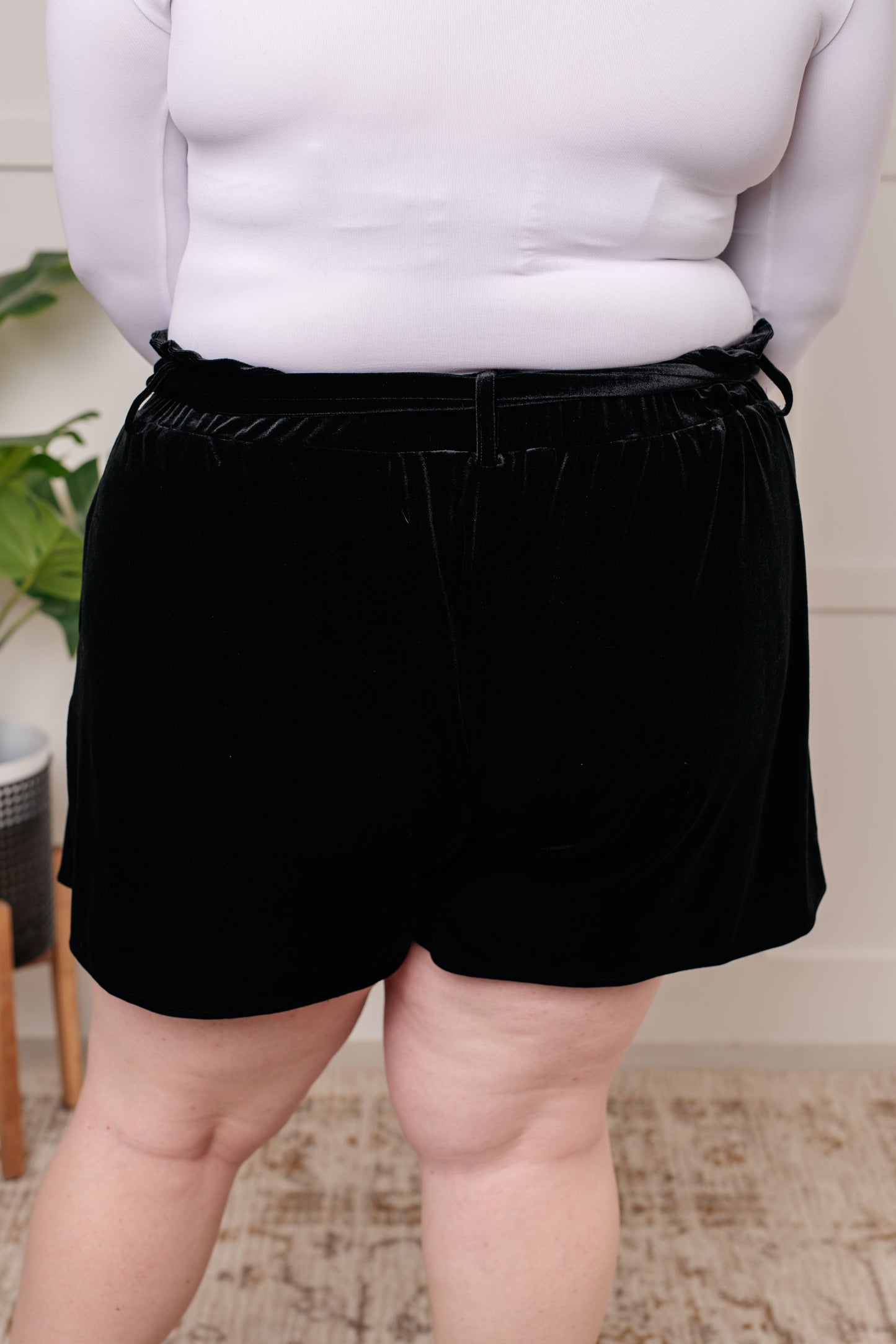 Wrapped in Velvet Shorts in black, featuring a high-rise elastic paper bag waistband, self-tie belt, and pockets for a stylish and adjustable fit.