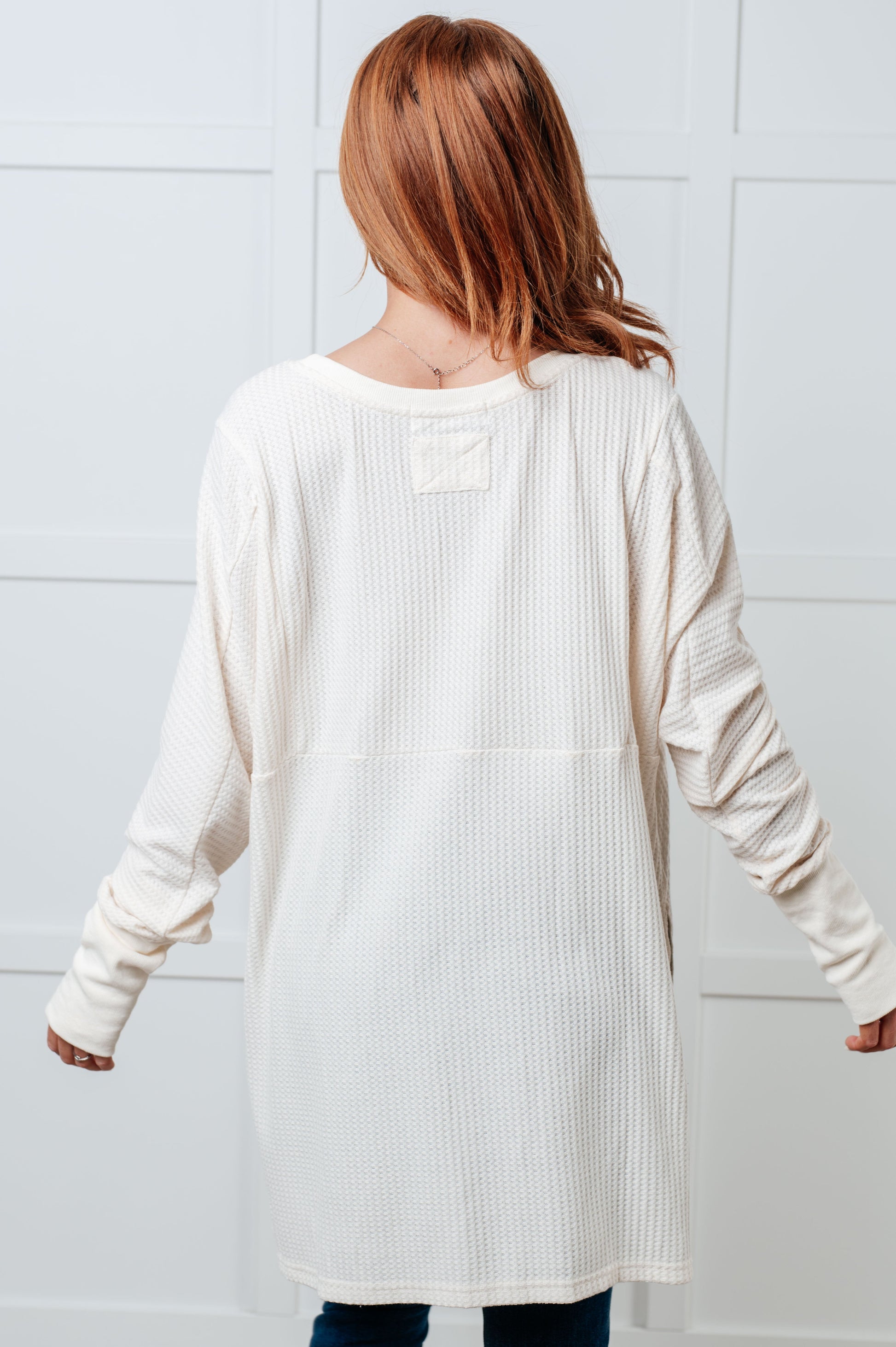 Women's waffle knit shirt with a scoop neckline, long sleeves, exaggerated contrast sleeve cuffs, asymmetrical hemline with side slits, and an oversized fit.