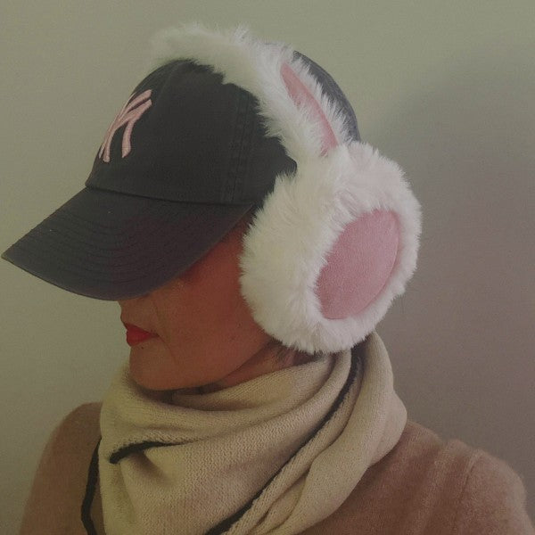 Woman wearing Snow Bunny Foldable Earmuffs in pink styled over a black cap for winter chic