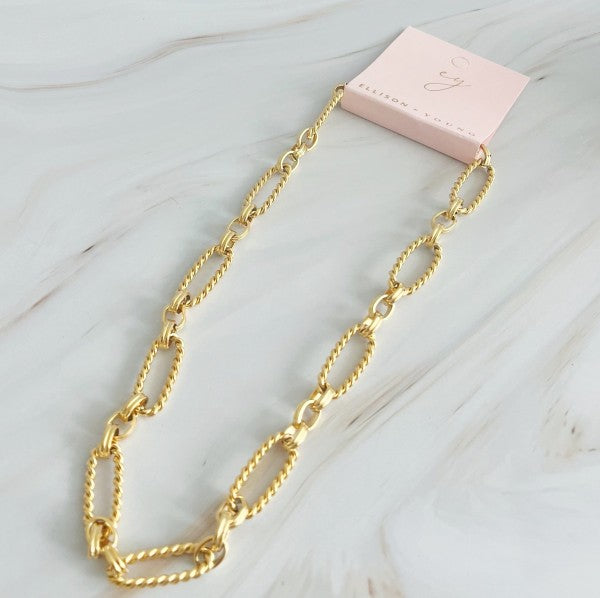 Gold alternatively linked cabled necklace on Ellison + Young pink branded card