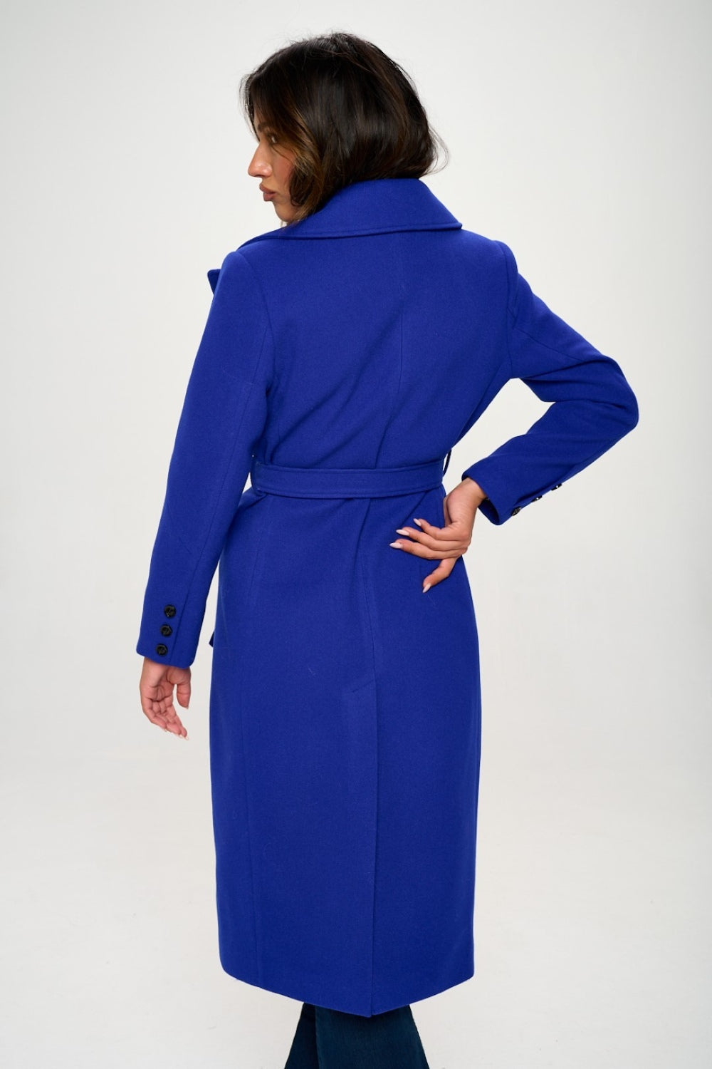 A royal blue double-breasted longline coat with a waist-cinching belt and long sleeves. The coat features a collared neckline, pocket details, and a tied closure.