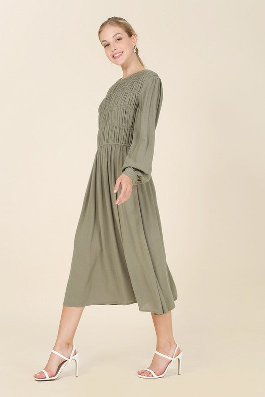 Olive midi dress with a boat neck, ruched bodice, long sleeves, and buttoned cuffs. Made from crinkle fabric.