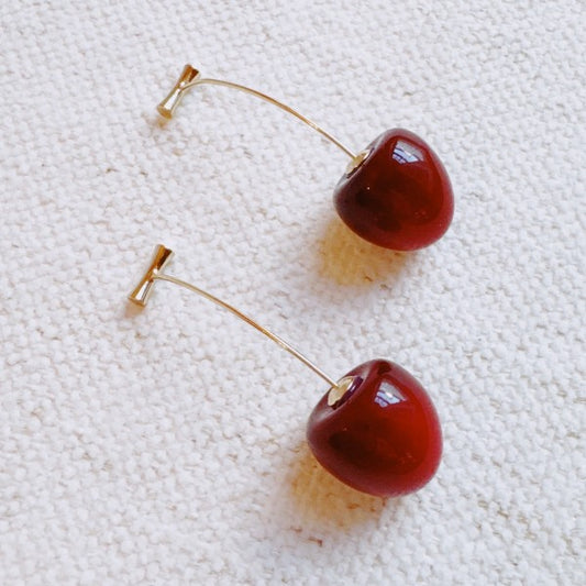 Sweet Cherry Drop Earrings with glossy red charms on gold bar design displayed on fabric background