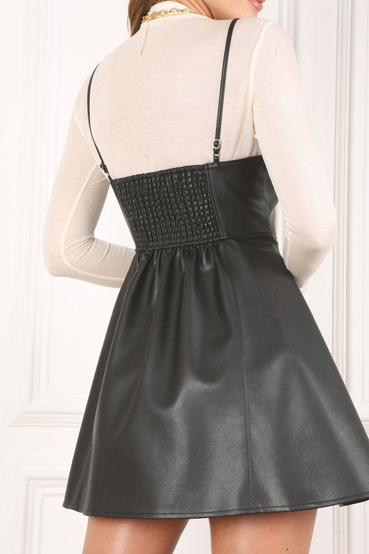 Black vegan leather mini dress with vertical cut lines at the front and back, smocking detail at the upper back, gathered waistline, and side zipper. Adjustable spaghetti straps for a custom fit.