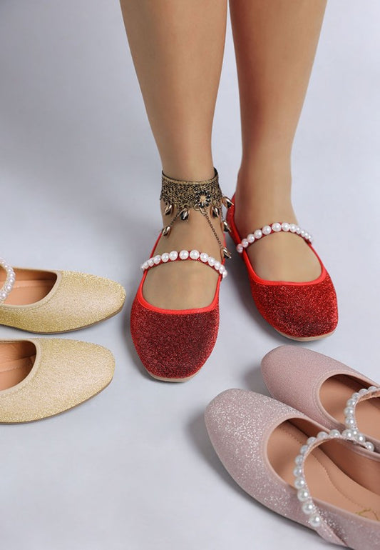 Woman wearing red Corphee Pearl Strapped Glitter Ballerinas with pink and gold pairs placed next to her feet.