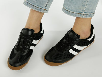 Top view of model wearing black Blaster sneakers with white stripes, showcasing lace-up design and breathable mesh upper by Rag Company
