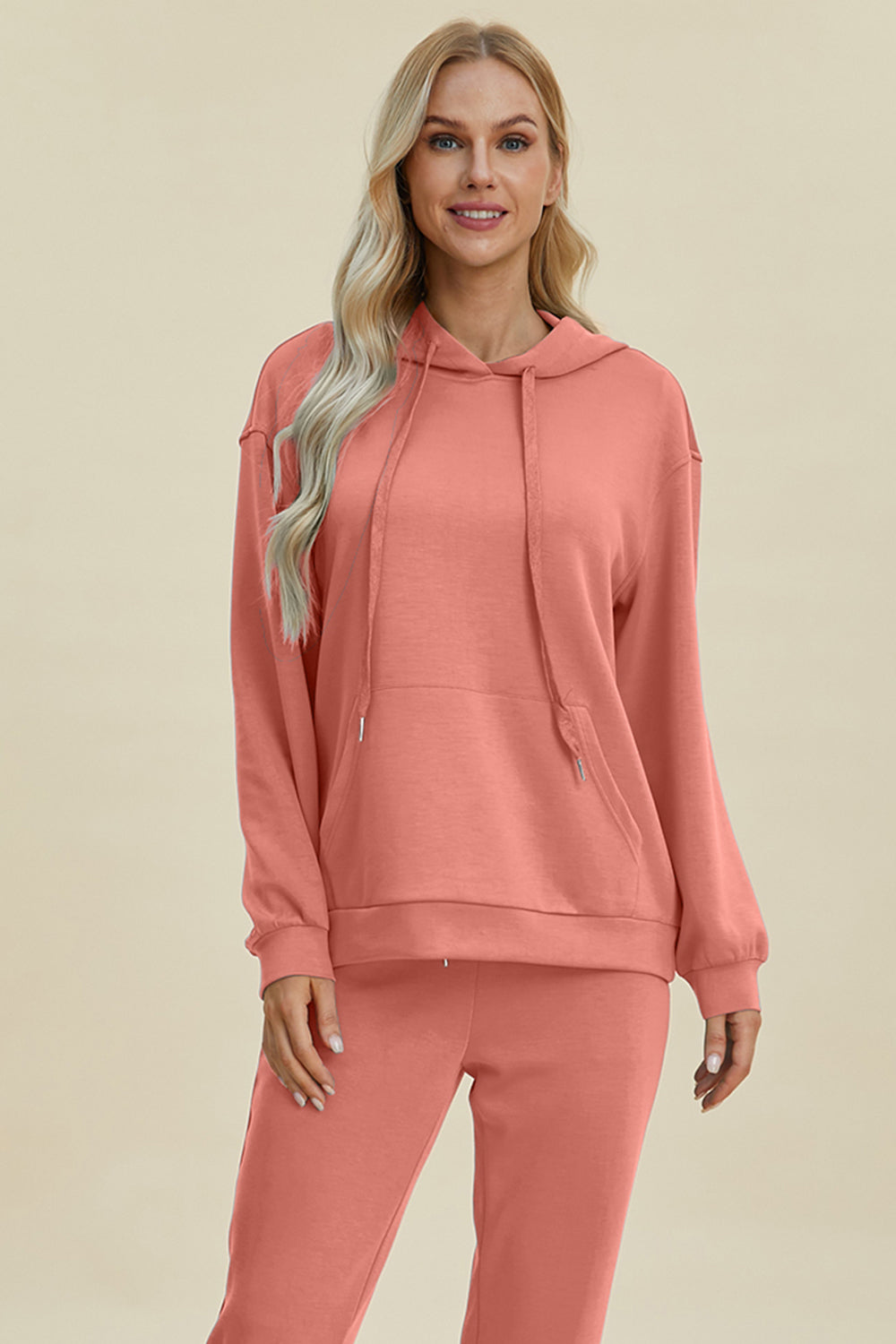 Coral long sleeve hoodie with kangaroo pocket, featuring a drawstring hood andrelaxed fit.