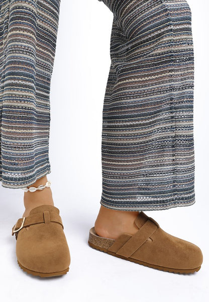 Model wearing Tan Ratiha Mules showing front and medial side view in faux suede finish.